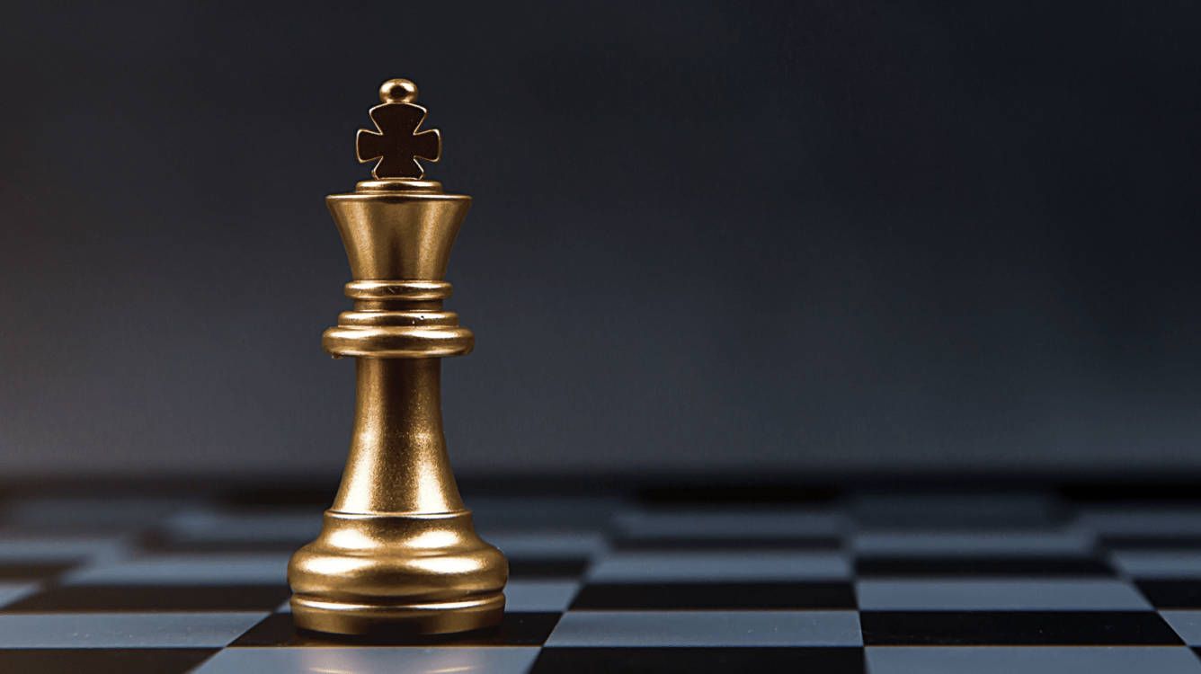 A gold king chess piece on a black and white chess board - Chess