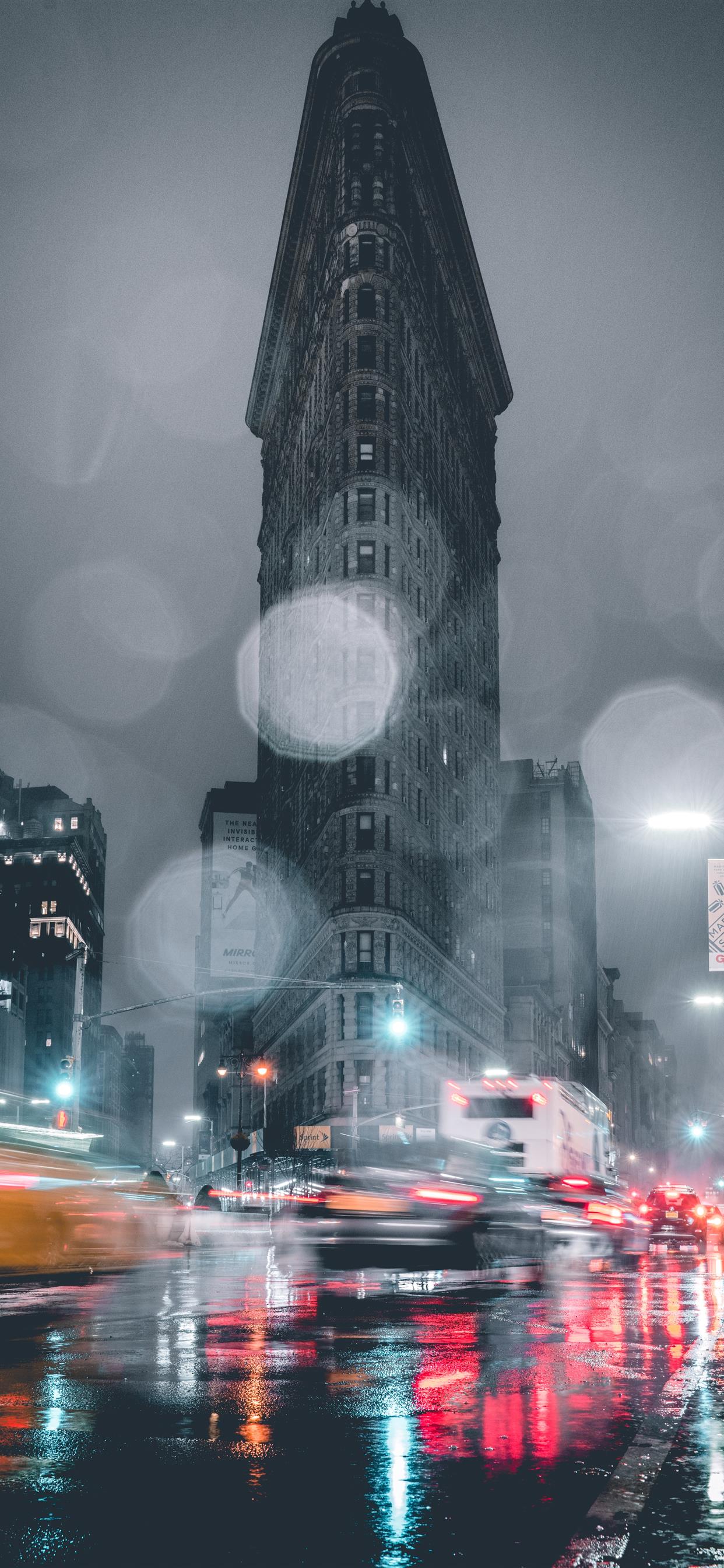 A car and a bus passing by the Flat Iron Building in the rain - Storm