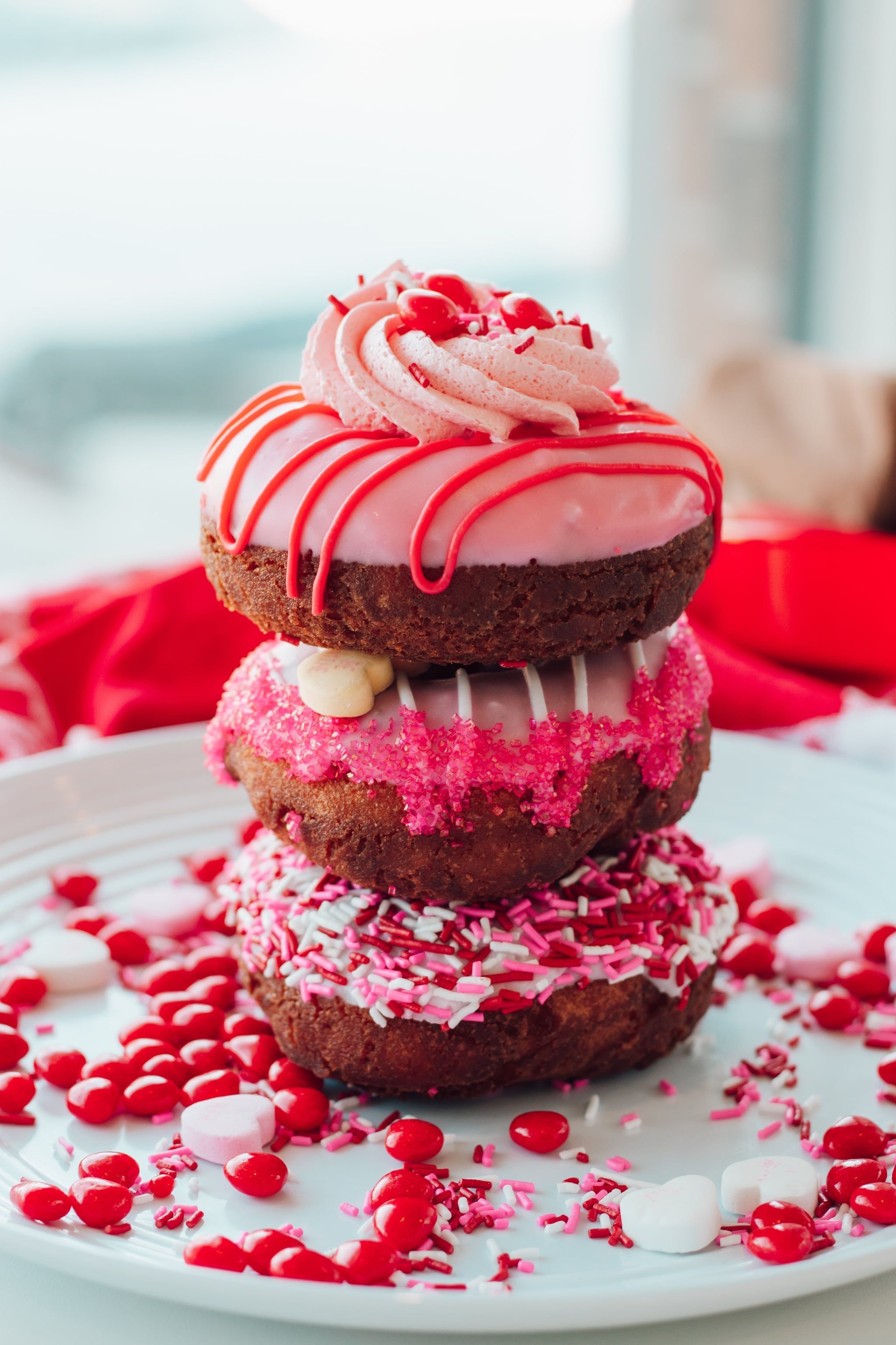 A stack of three Valentine's Day donuts on a plate. - Cake