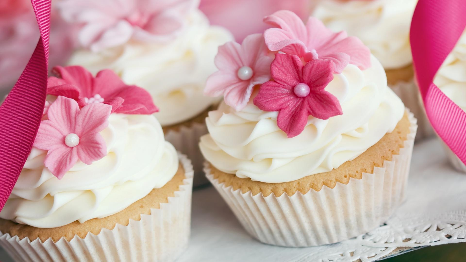 A collection of cupcakes with white frosting and pink flowers on top. - Cake