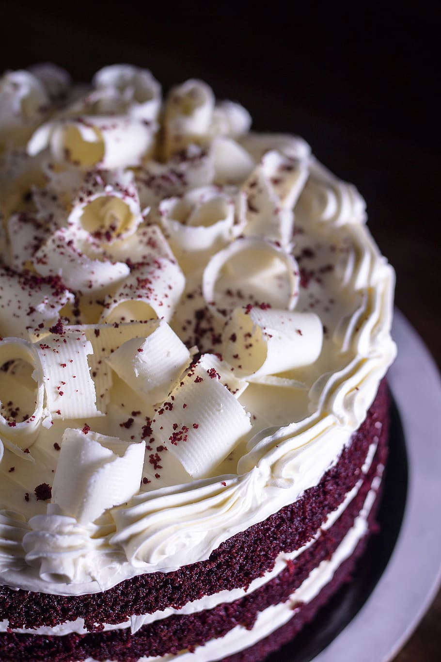 A red velvet cake with white icing on a plate. - Cake