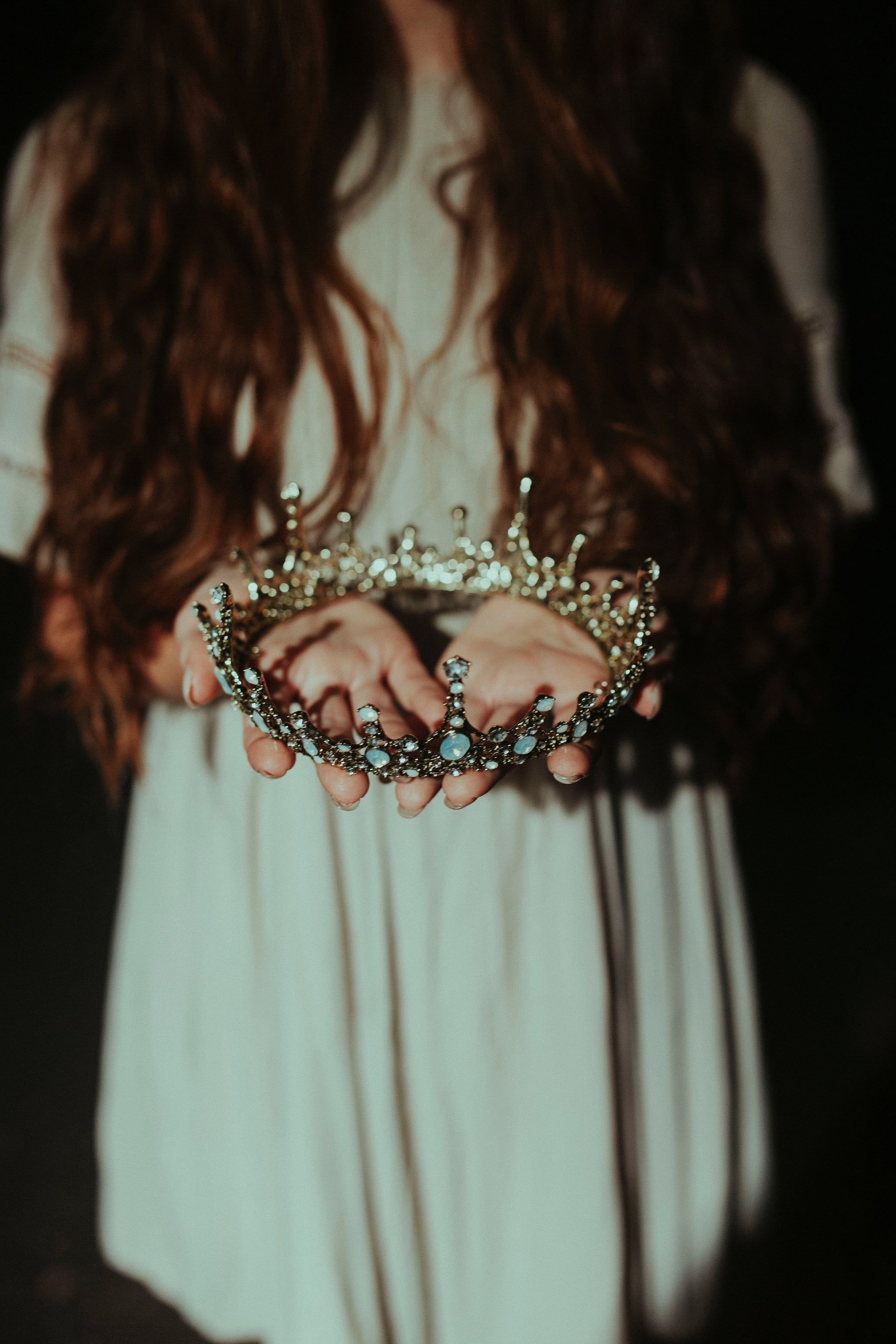 A woman with long brown hair holding a silver crown. - Crown, royalcore