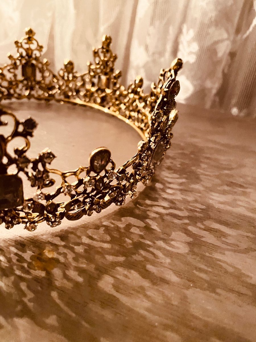 A gold crown with jewels sits on a white surface. - Crown, gold
