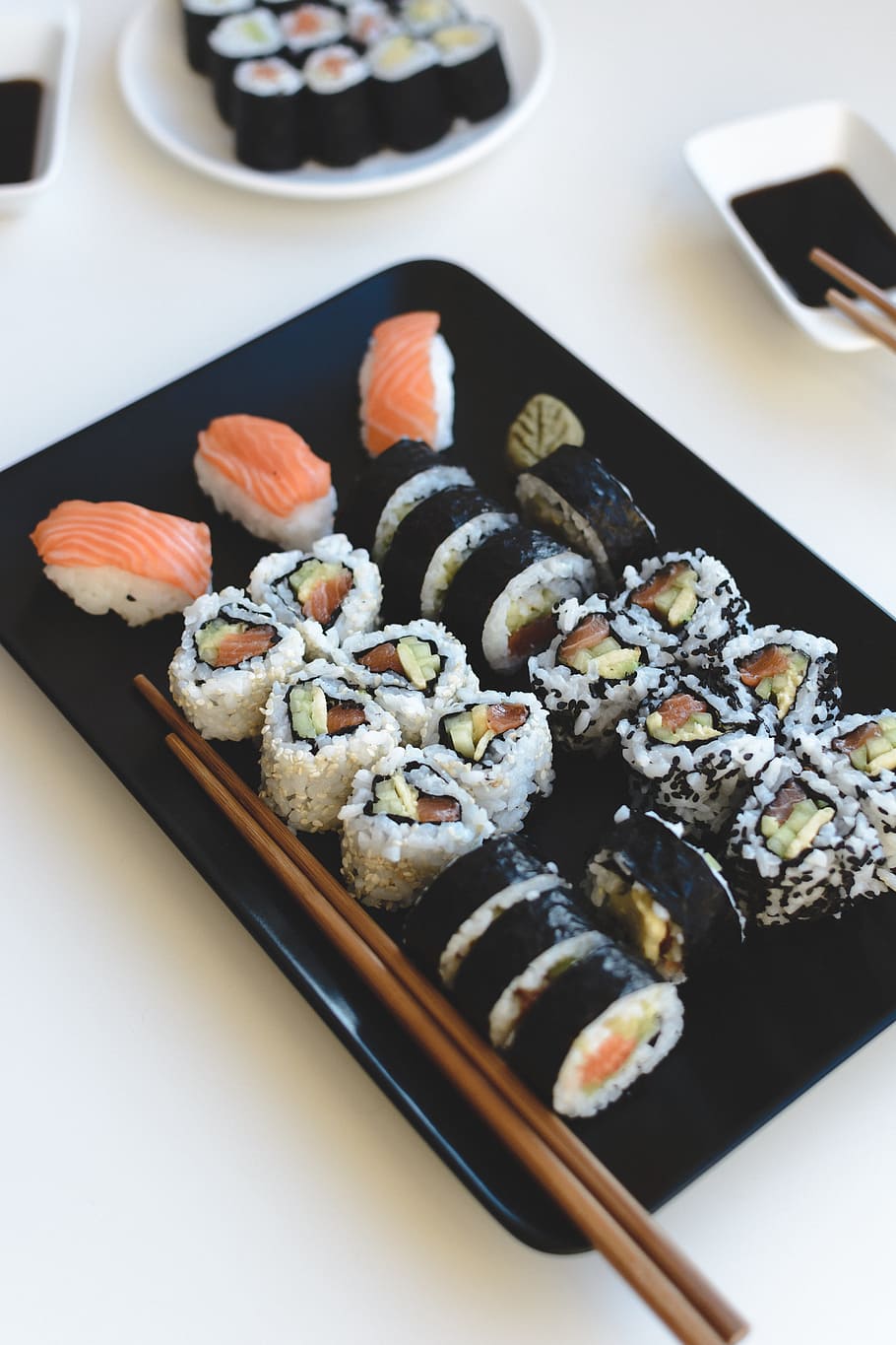 A plate of sushi with chopsticks on a white table. - Sushi