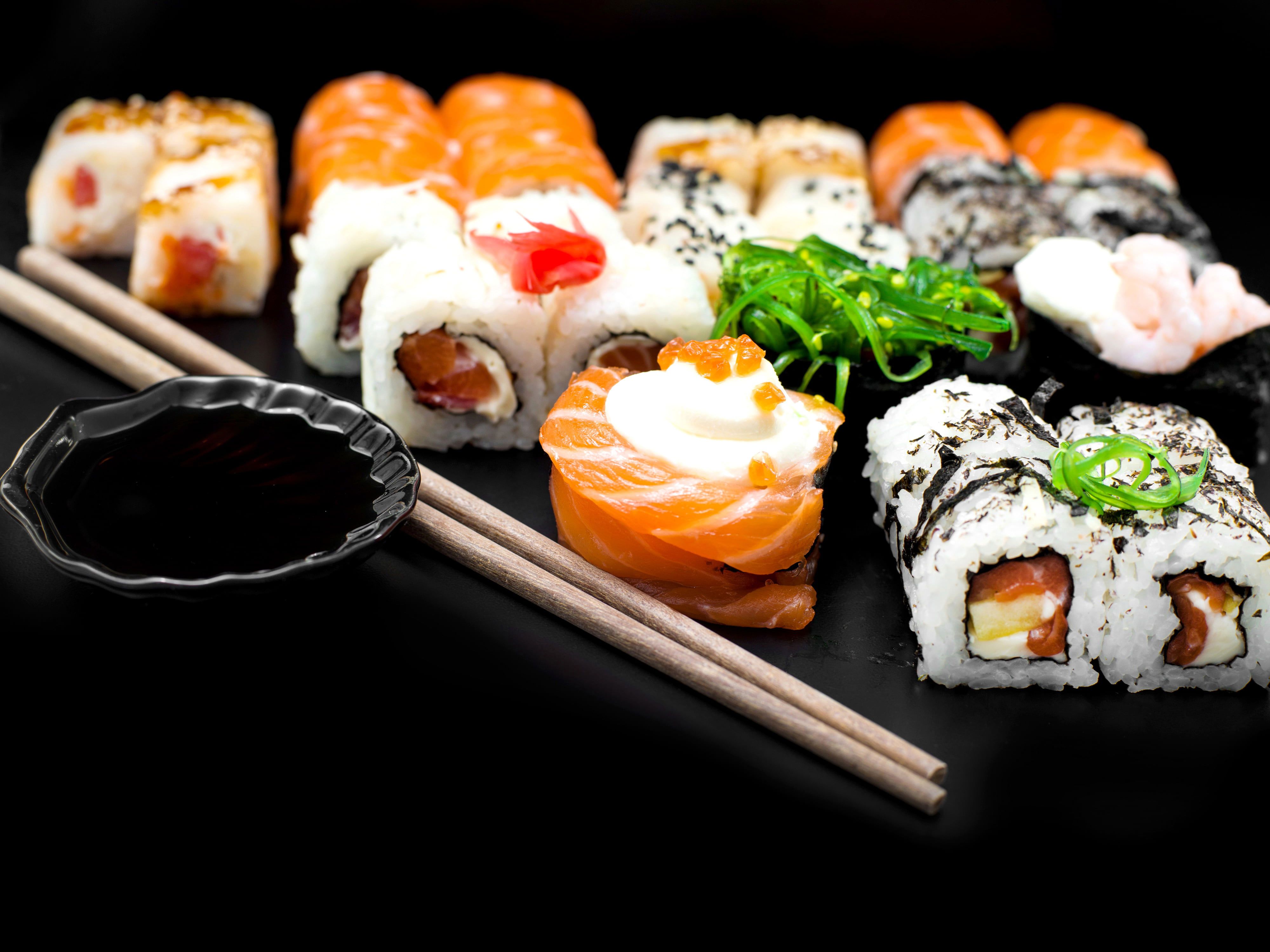 Various types of sushi on a black plate with chopsticks and soy sauce. - Sushi