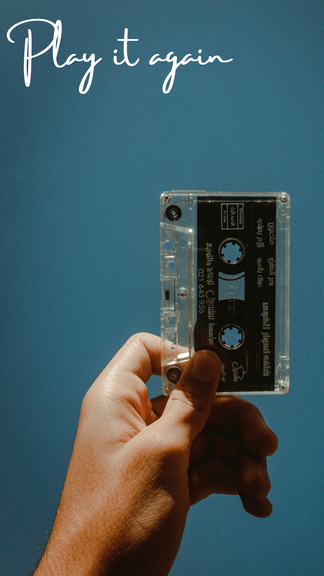 A hand holding a cassette tape against a blue background - Phone