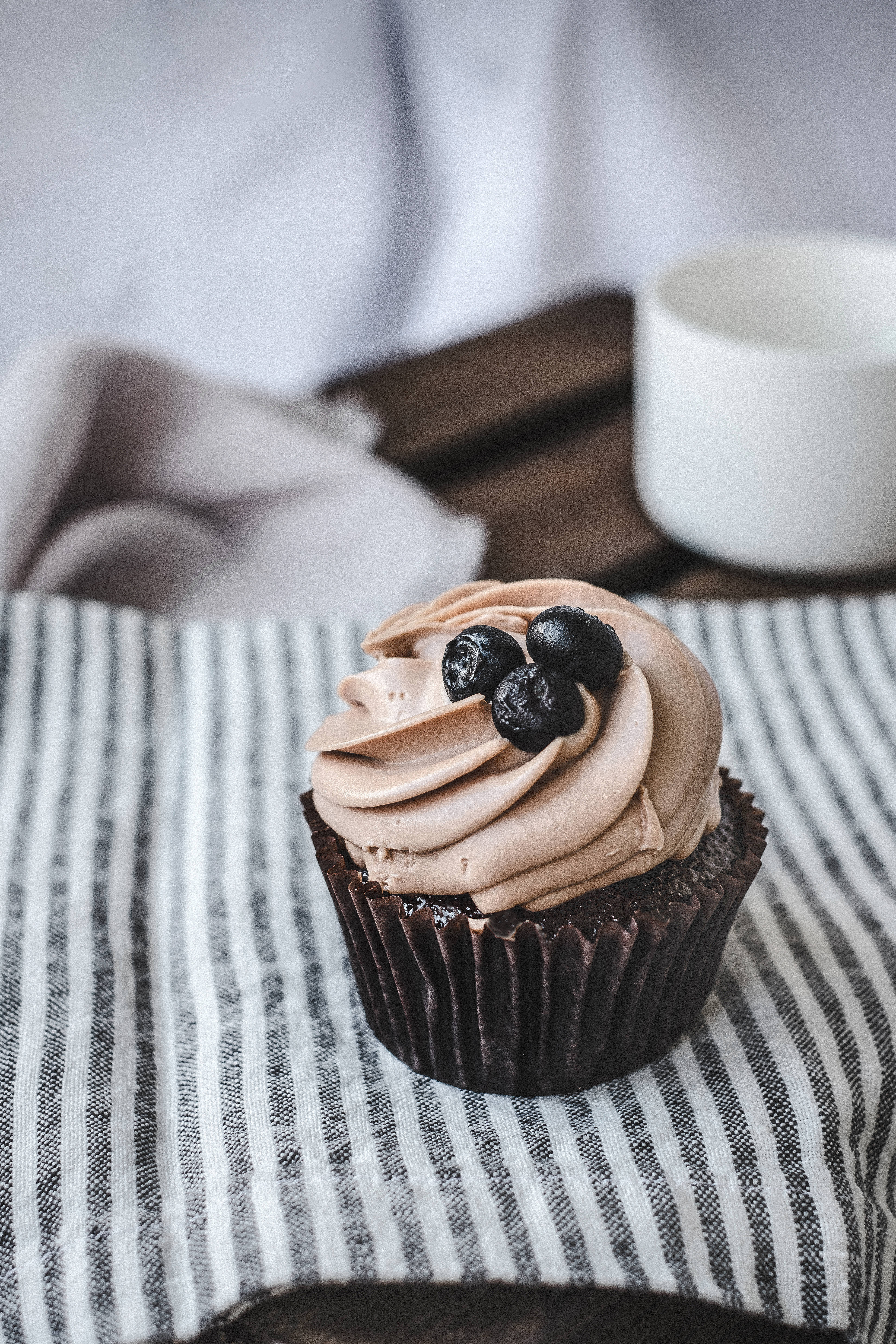 A chocolate cupcake with chocolate frosting and blueberries on top. - Cupcakes