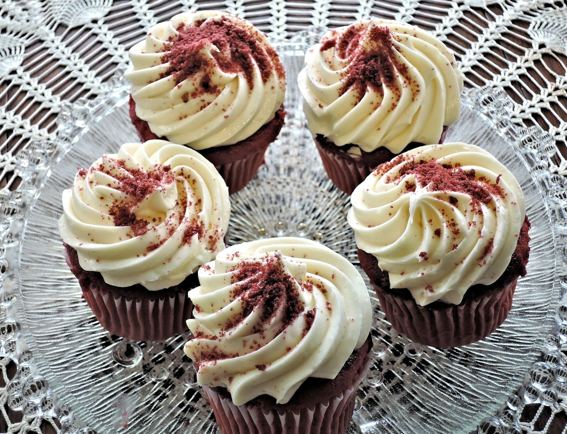 Four cupcakes with white icing and red sprinkles on a glass plate. - Cupcakes