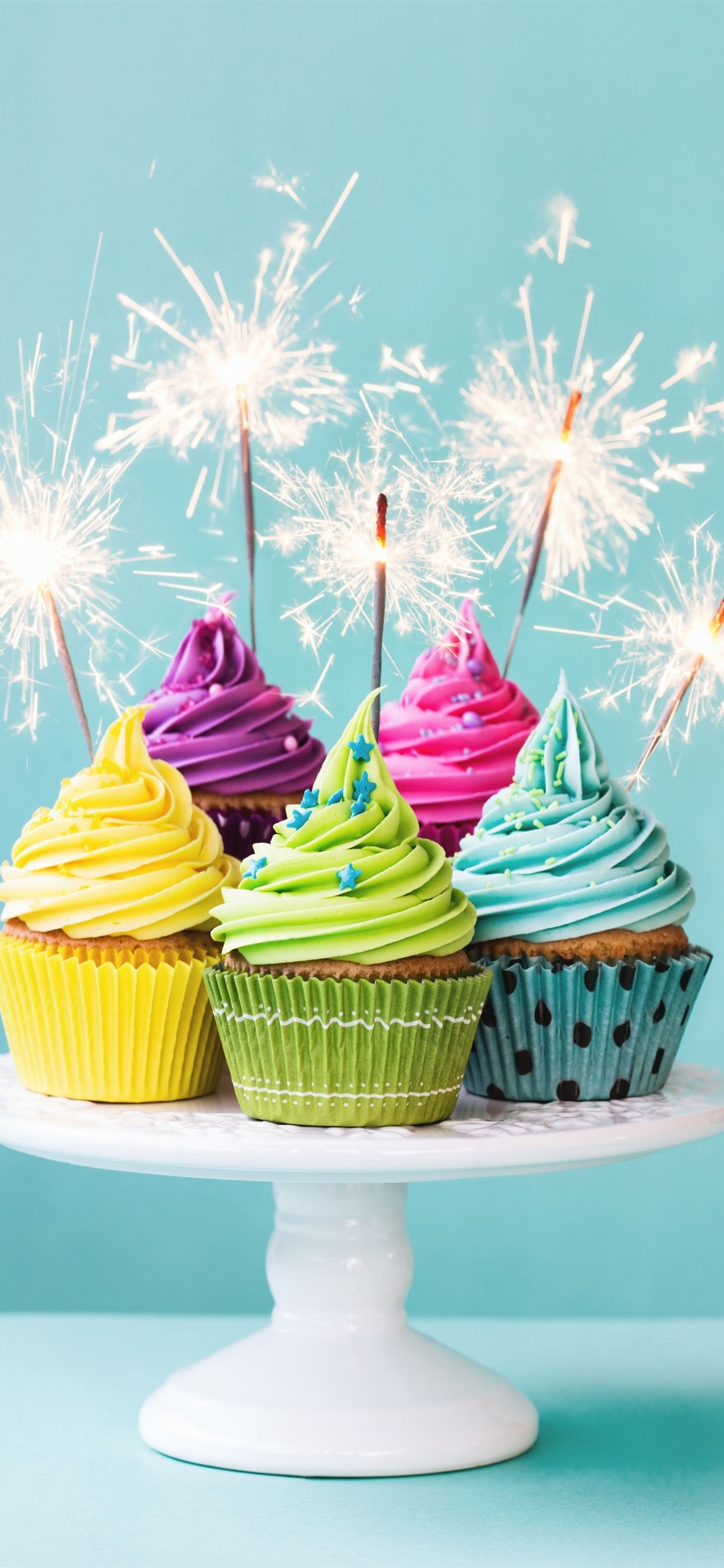 A plate of cupcakes with colorful icing and sparklers. - Cupcakes