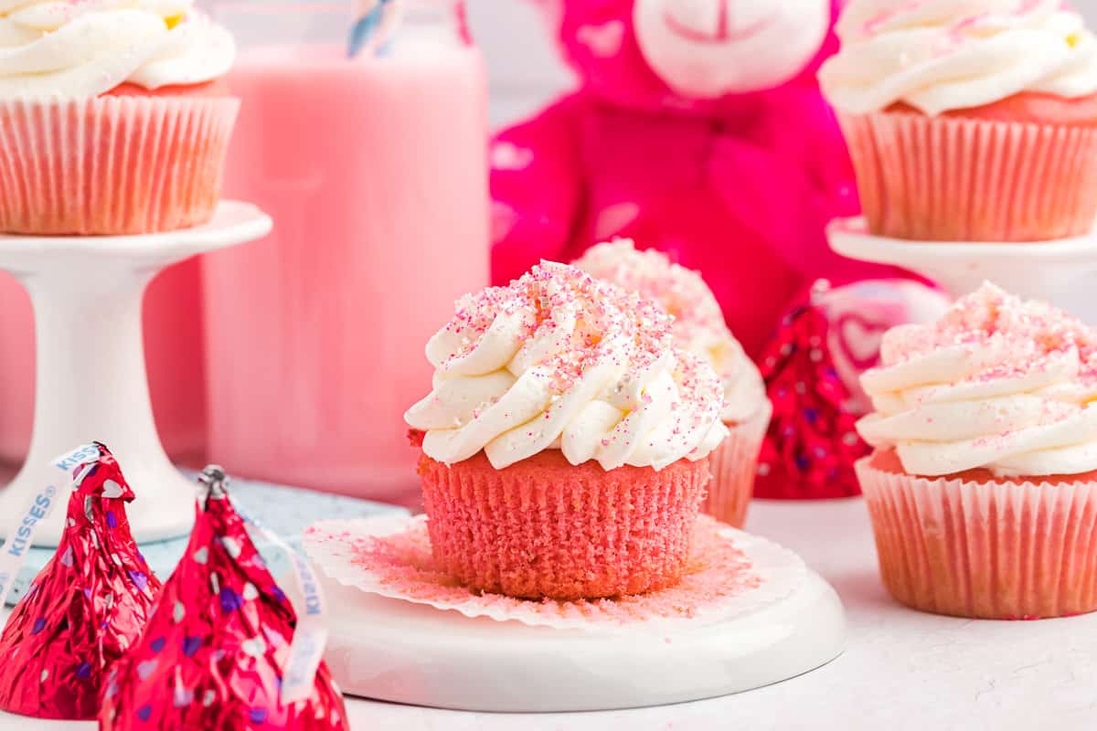 Pink cupcakes with white frosting and pink sprinkles on a white plate. - Cupcakes