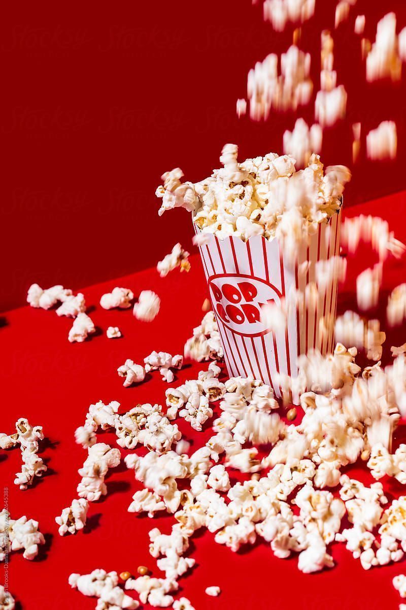 Popcorn falling out of a popcorn bucket onto a red surface - Popcorn