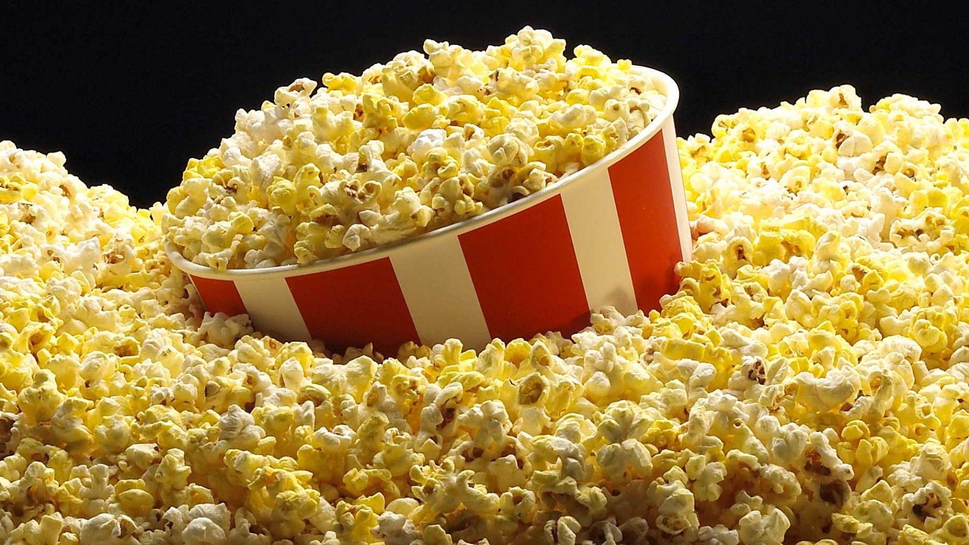 A red and white bucket of popcorn is surrounded by popcorn. - Popcorn