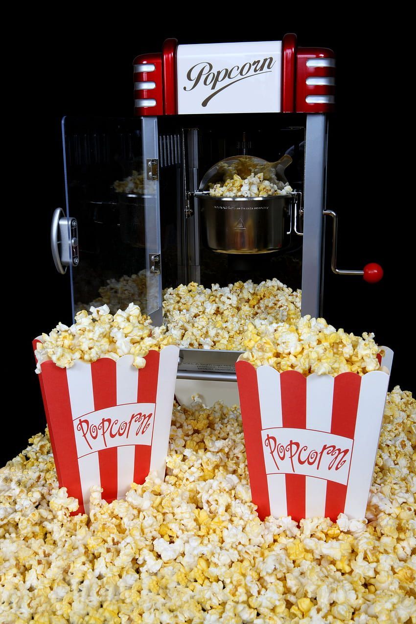 Two red and white striped popcorn buckets filled with popcorn in front of a popcorn maker - Popcorn