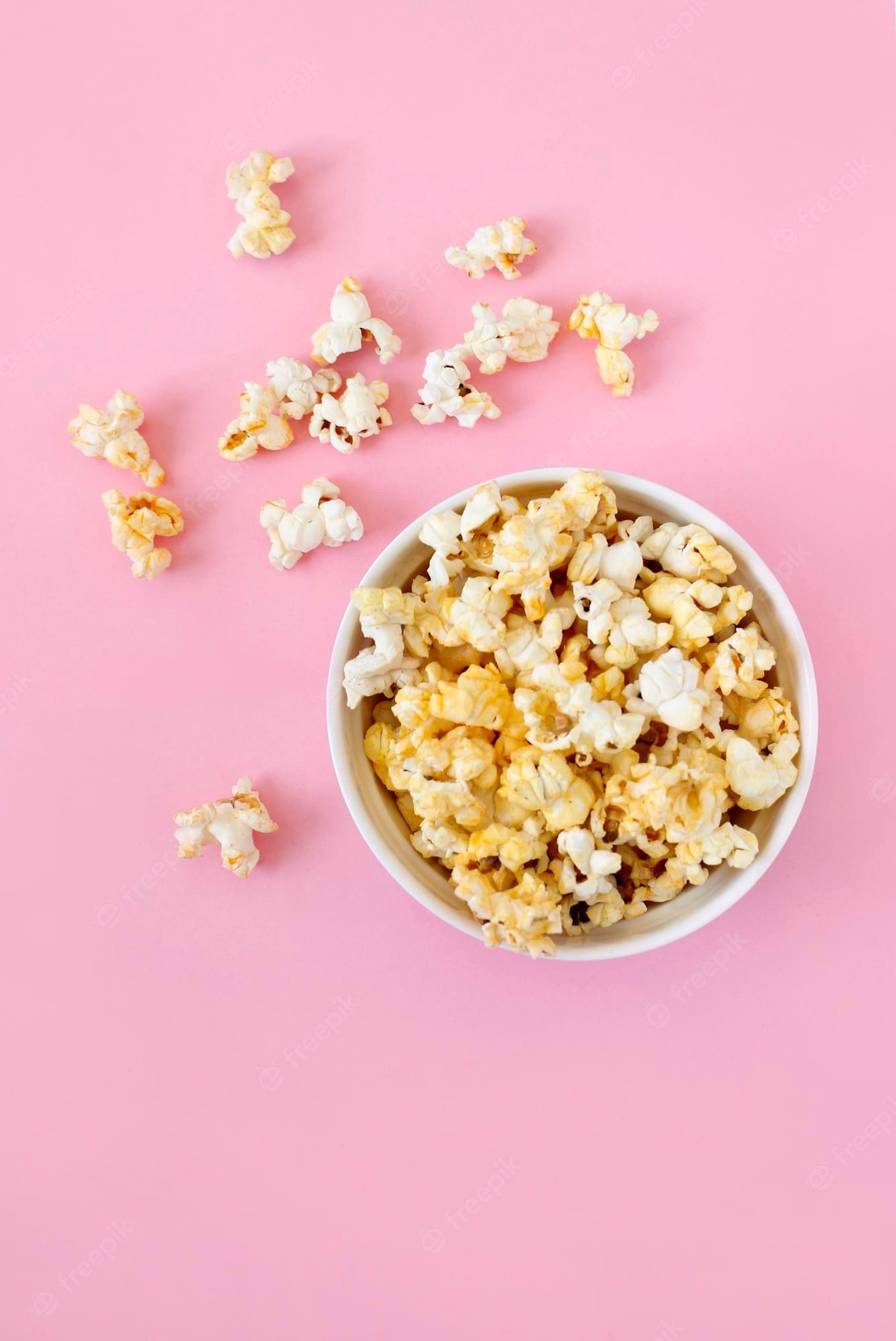 Premium Photo. Spilled popcorn on pink background movie night concept copy space for text