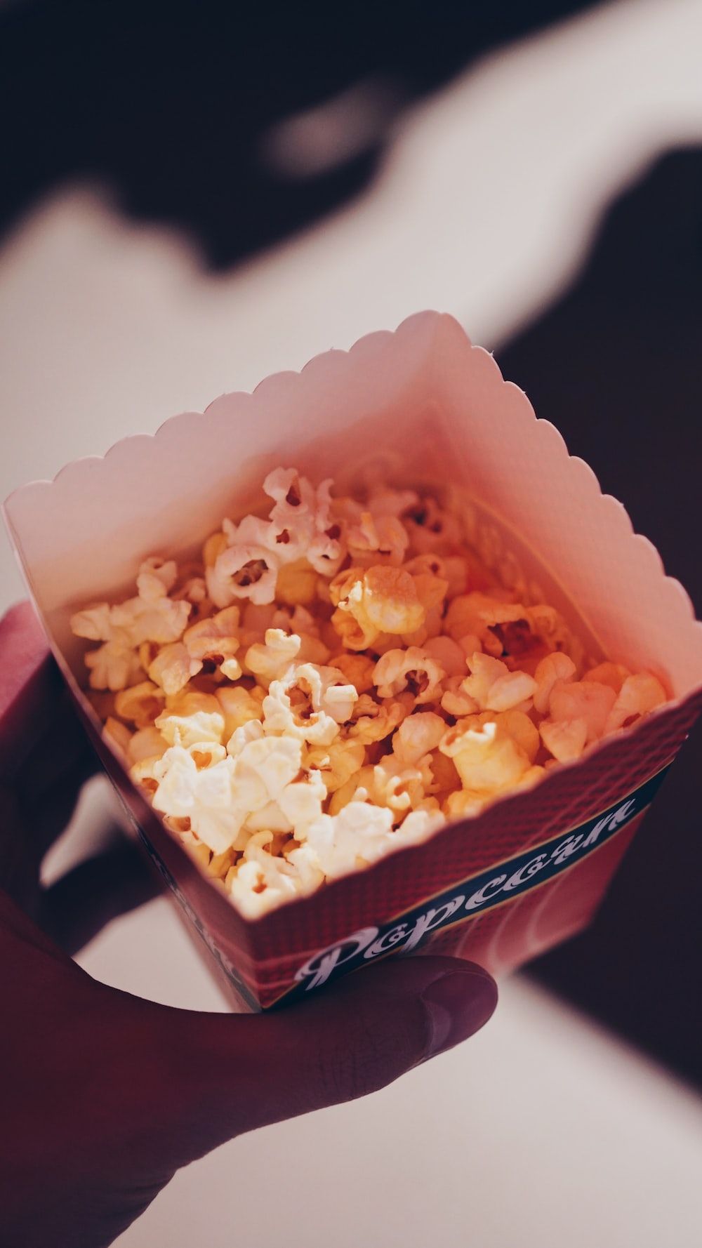 A box of popcorn is being held by a person. - Popcorn