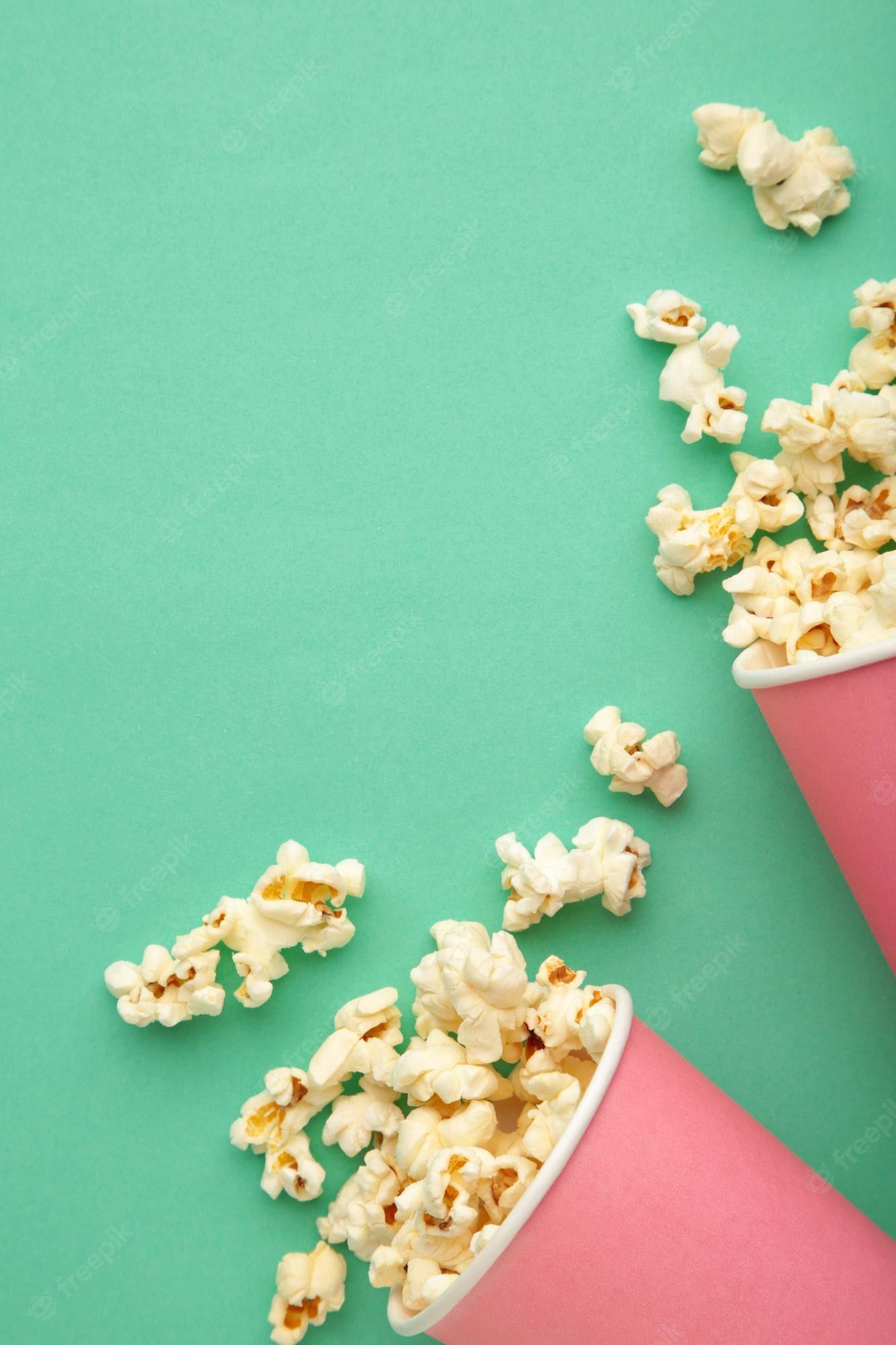 Popcorn spilling out of a pink paper cup on a green background - Popcorn