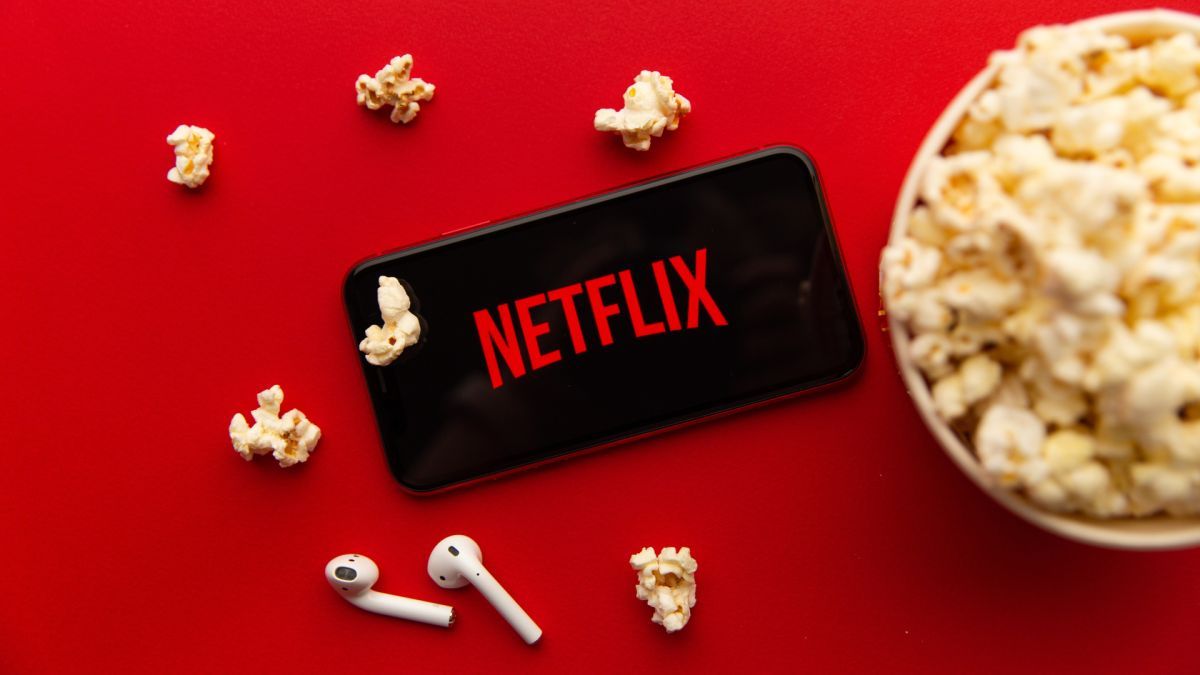 Netflix logo on a phone screen surrounded by popcorn and earphones - Popcorn, Netflix