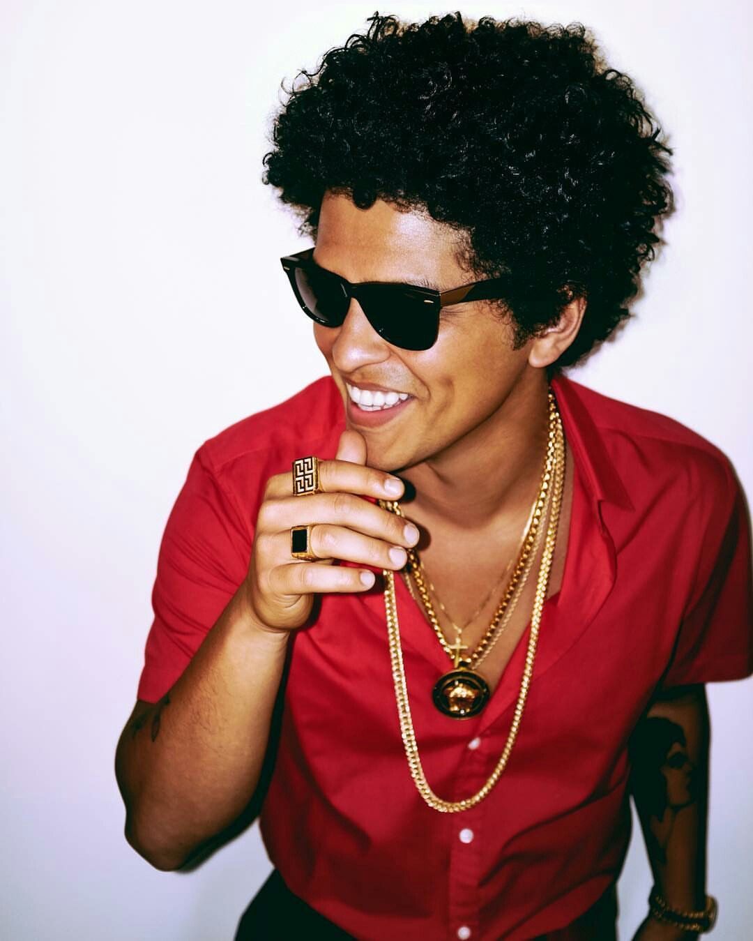 A man in sunglasses and red shirt holding his phone - Bruno Mars