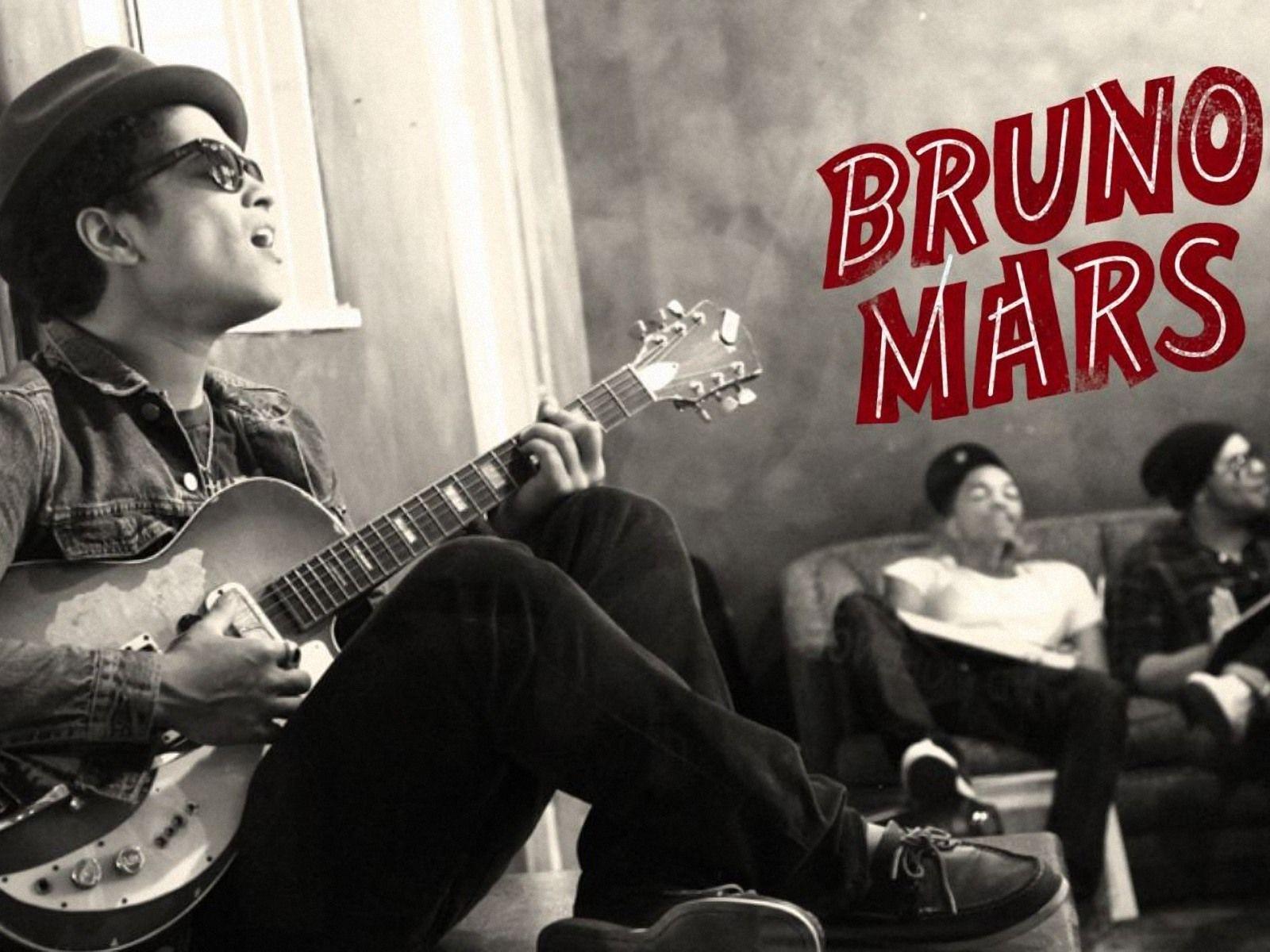 Bruno Mars playing a guitar with two other men in the background. - Bruno Mars