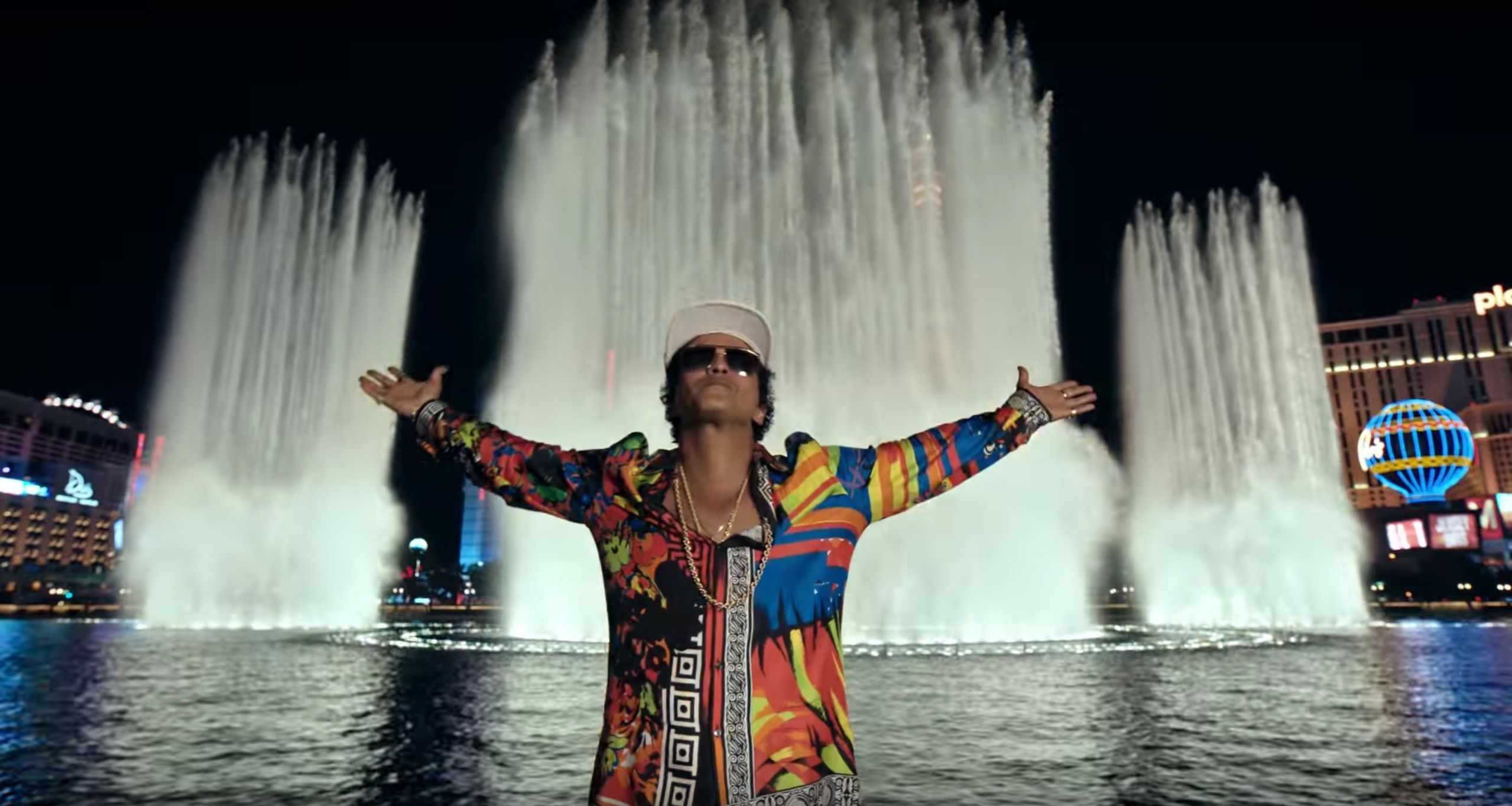 Bruno Mars stands in front of the Bellagio fountain in Las Vegas, with his arms outstretched, in the music video for 