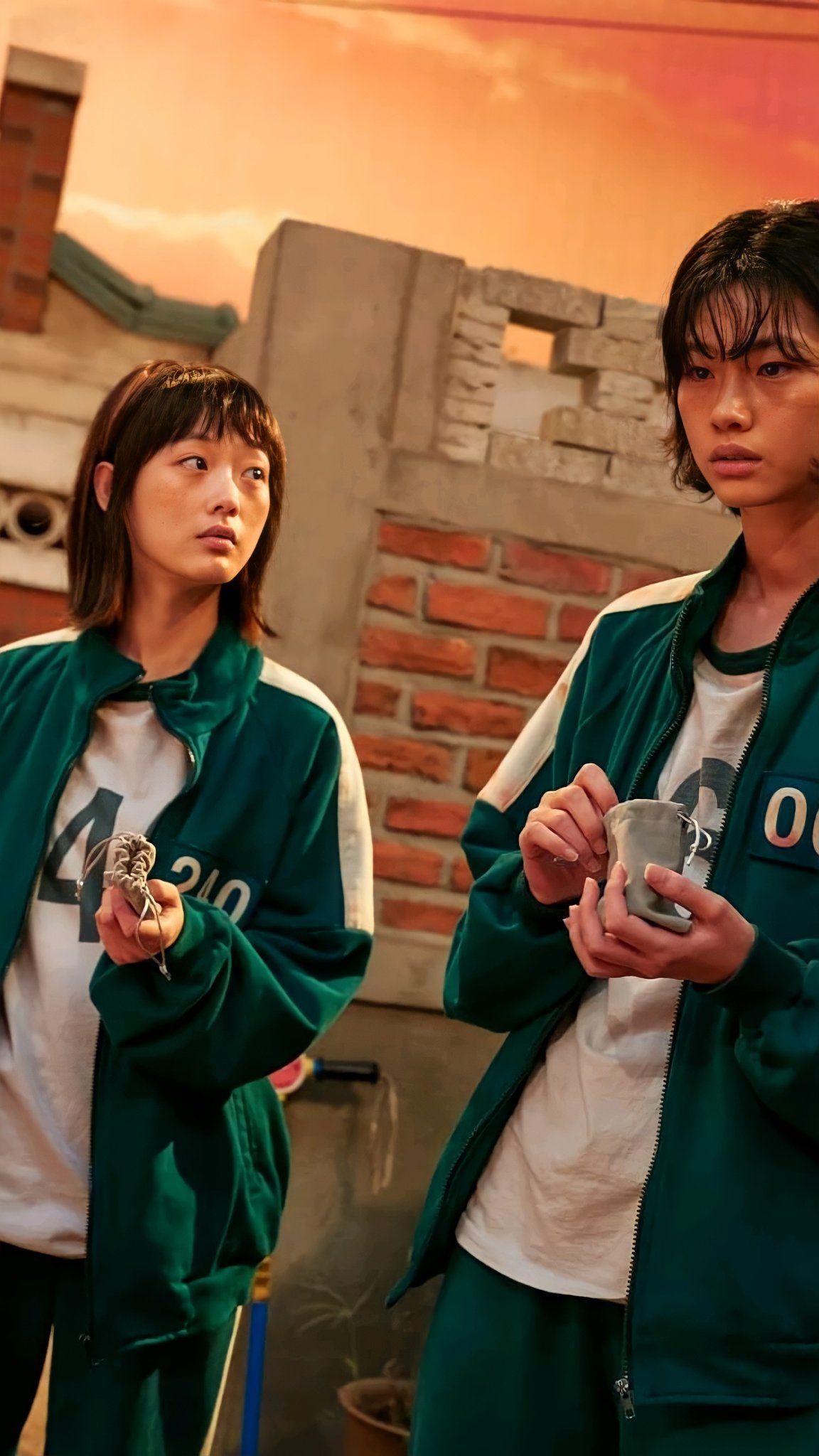 A still from the drama 'Tale of the Nine-Tailed'. Two women stand side by side, both wearing green tracksuits. - Squid Game