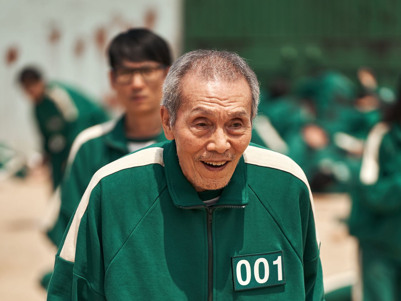 An older man wearing a green track suit with the number 001 on it - Squid Game