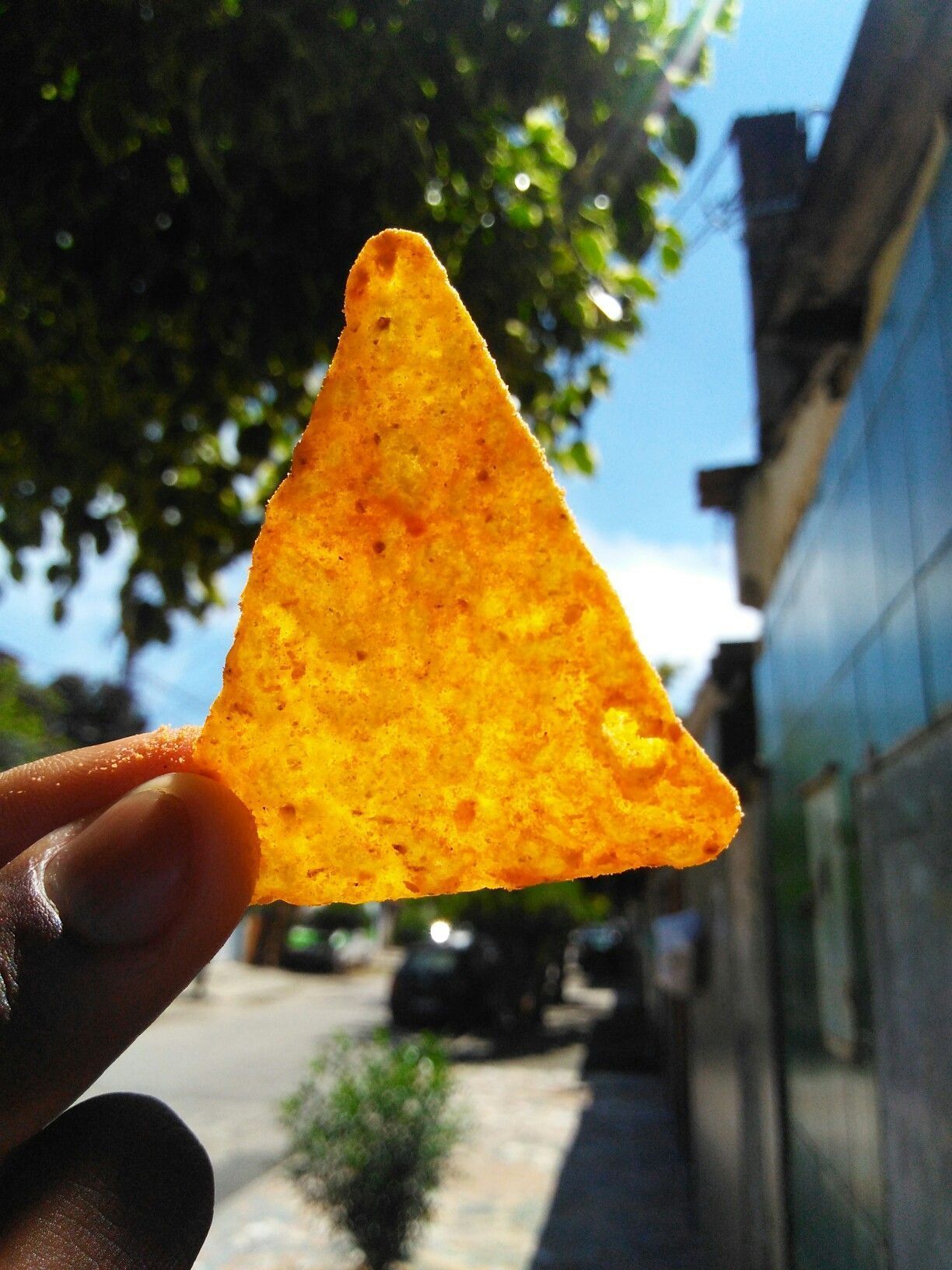 A hand holding a yellow triangle shaped food - Doritos