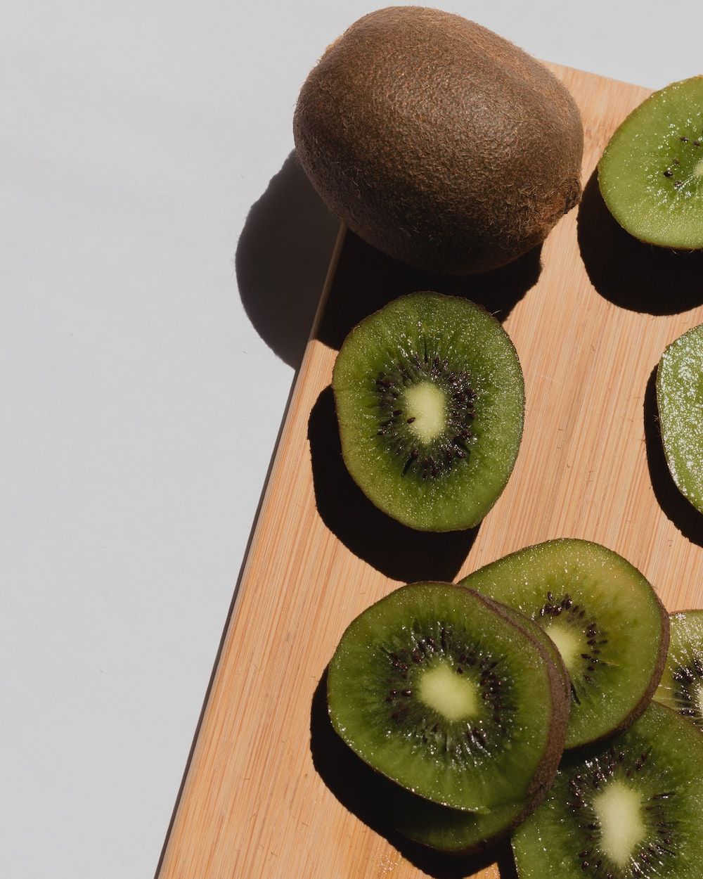 A wooden cutting board with sliced kiwi on top. - Kiwi