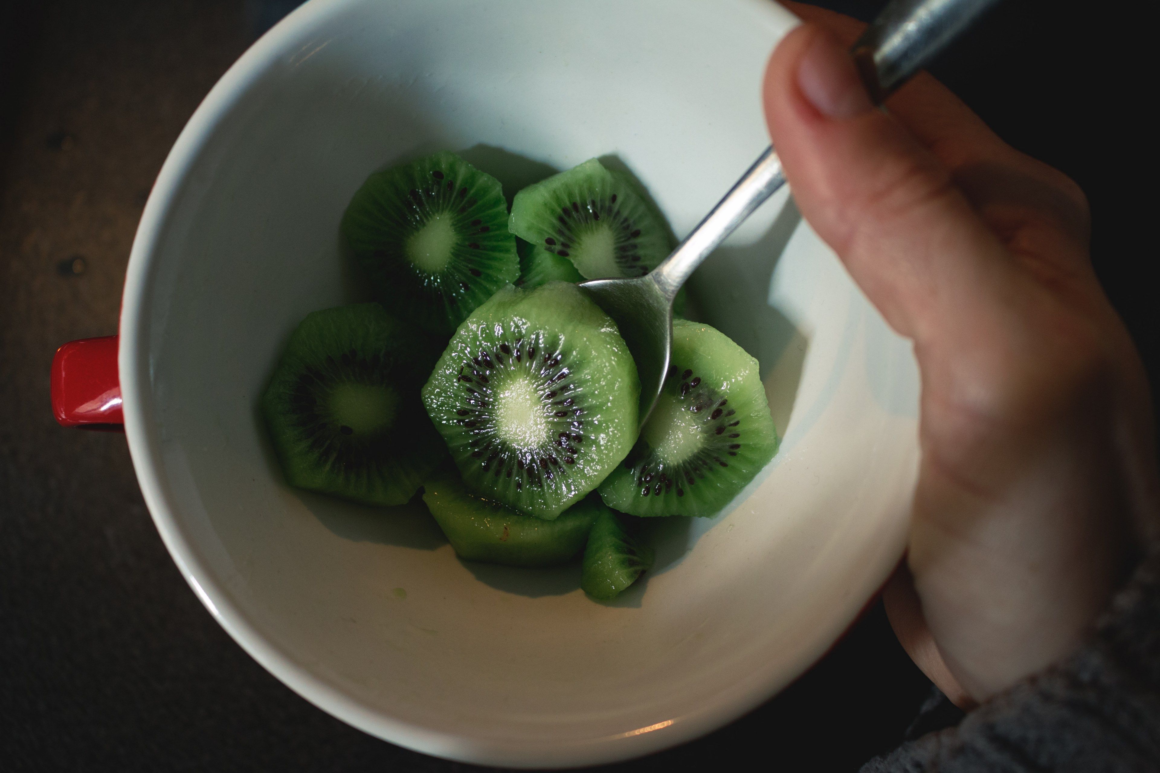 A person is holding a spoon in a bowl of kiwi slices. - Kiwi