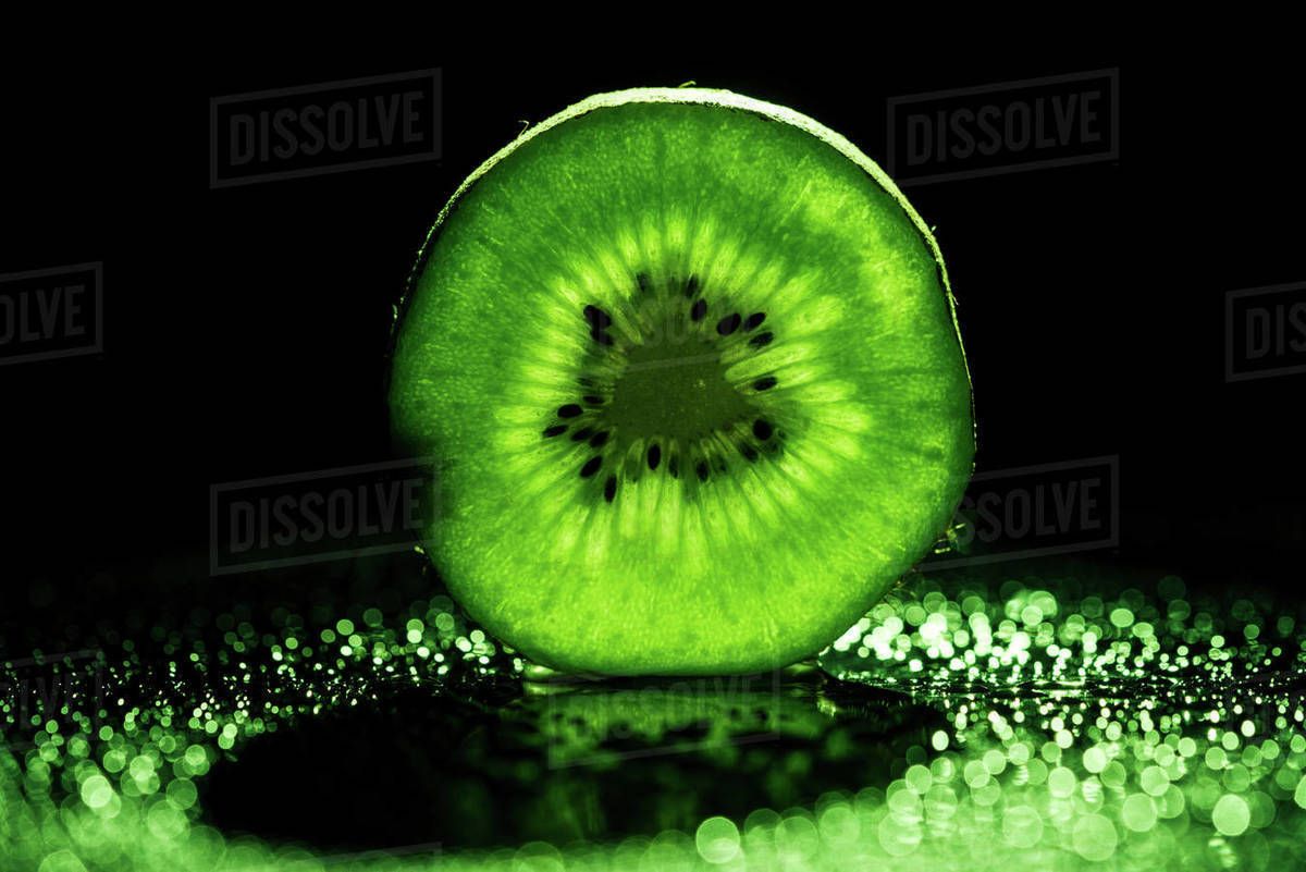 Slice of kiwi fruit on black background with neon green backlit