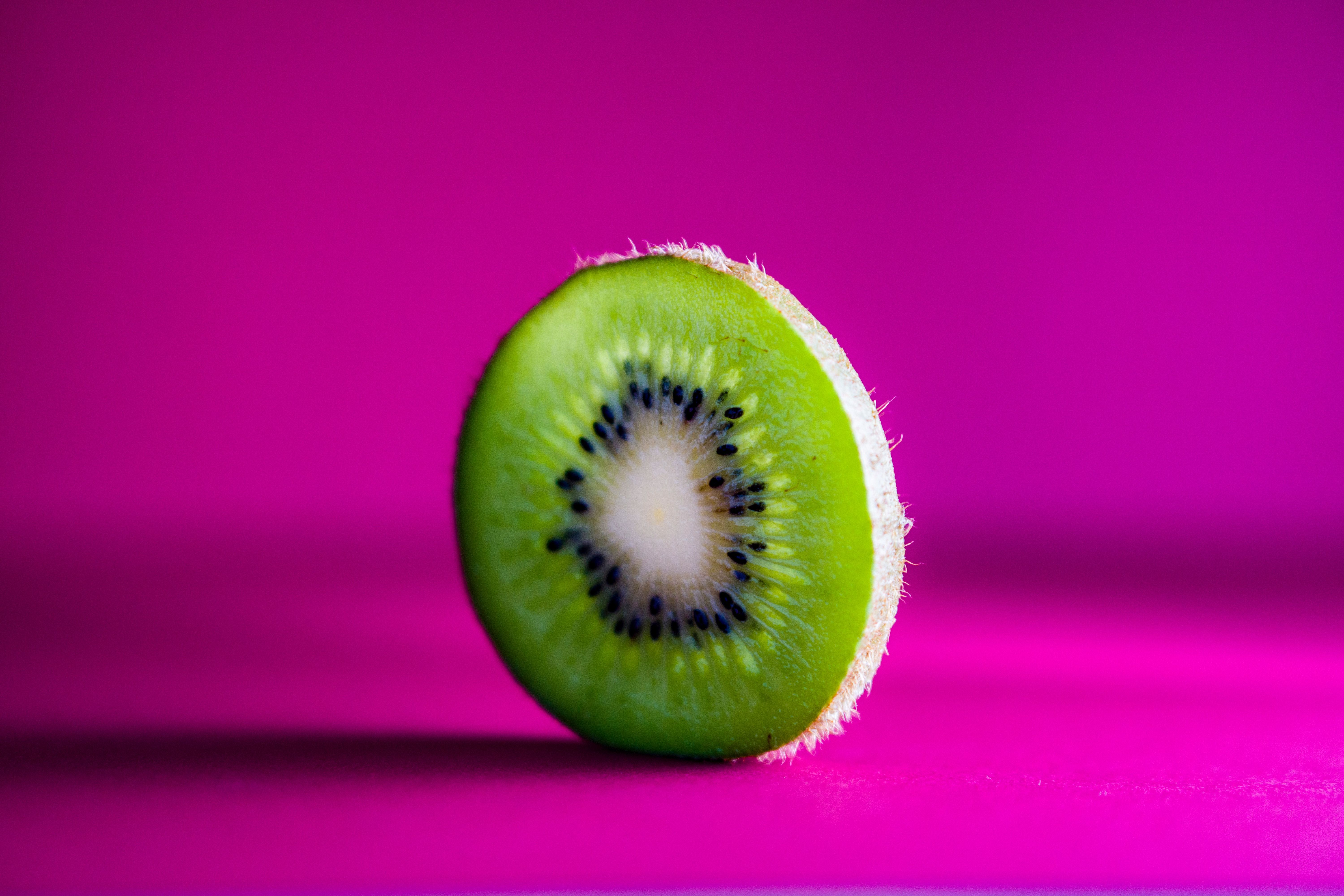 A kiwi fruit sitting on top of pink background - Kiwi