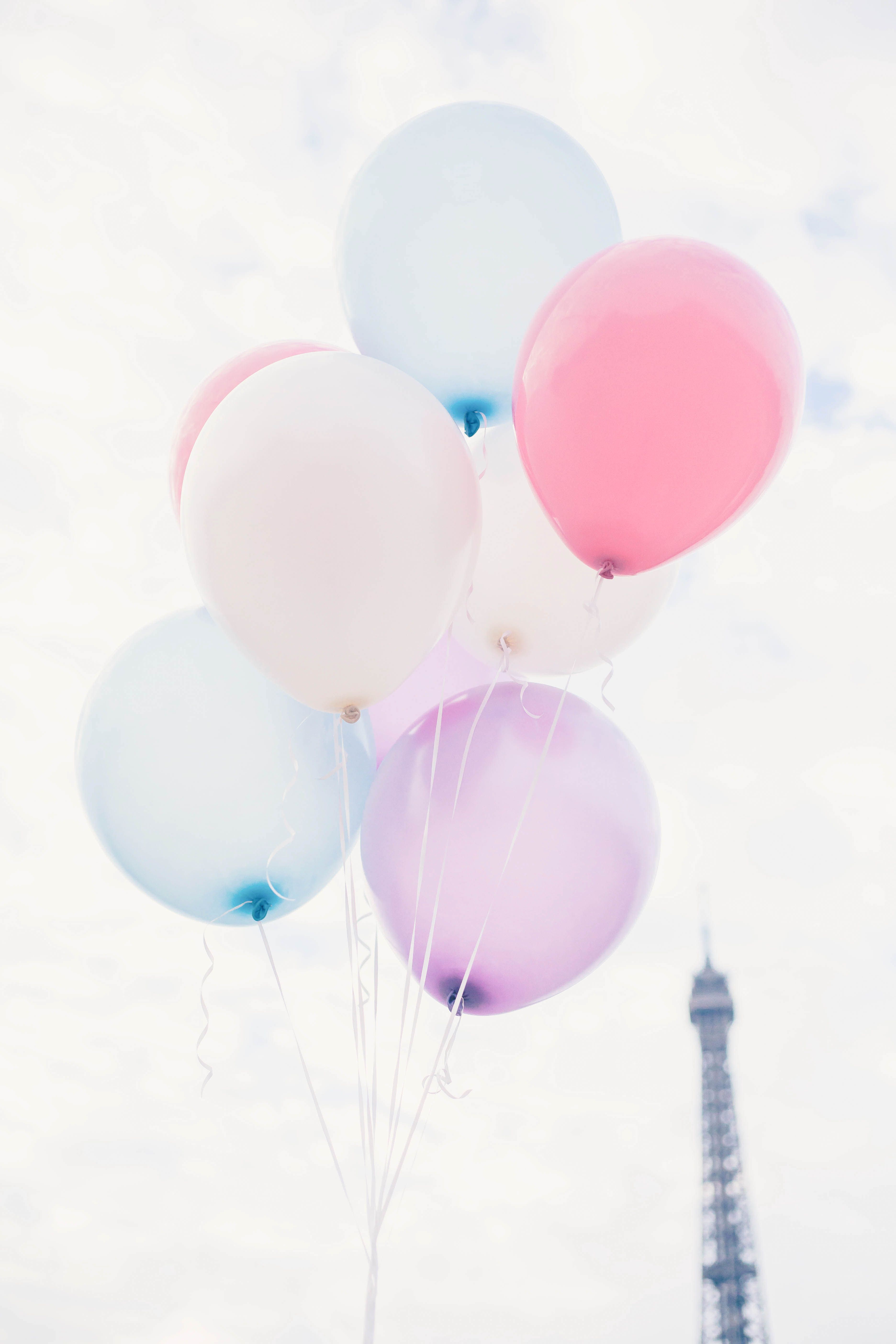 Pink, purple, and blue balloons floating in the sky with the Eiffel Tower in the background. - Balloons