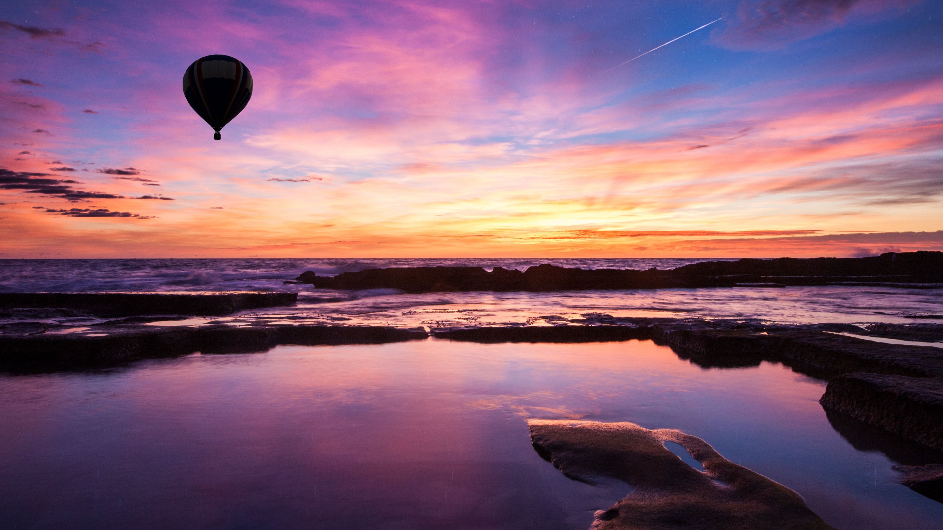 Hot air balloon flying over the ocean during a colorful sunset - Hot air balloons