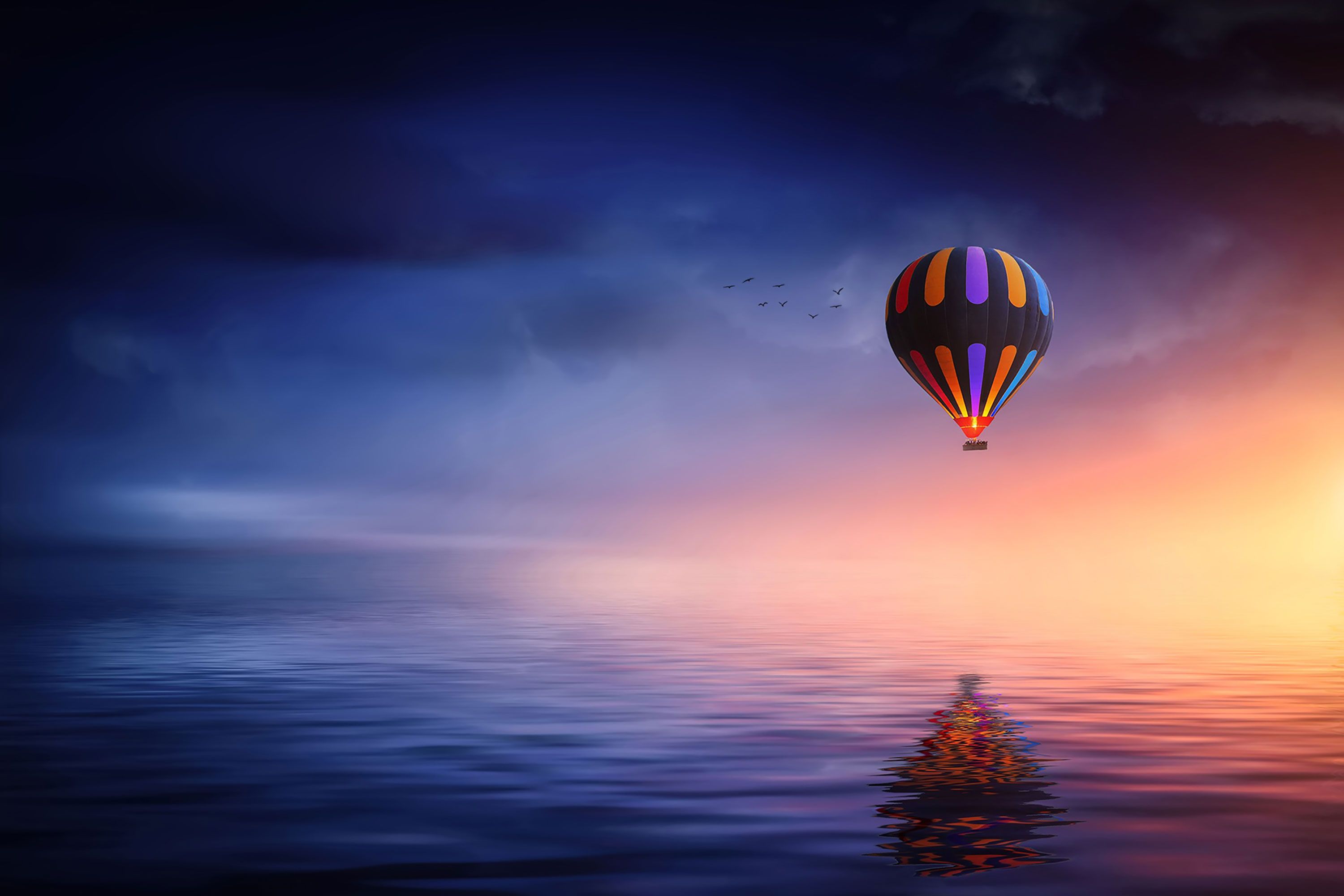 A hot air balloon flies over a calm sea at sunset - Hot air balloons