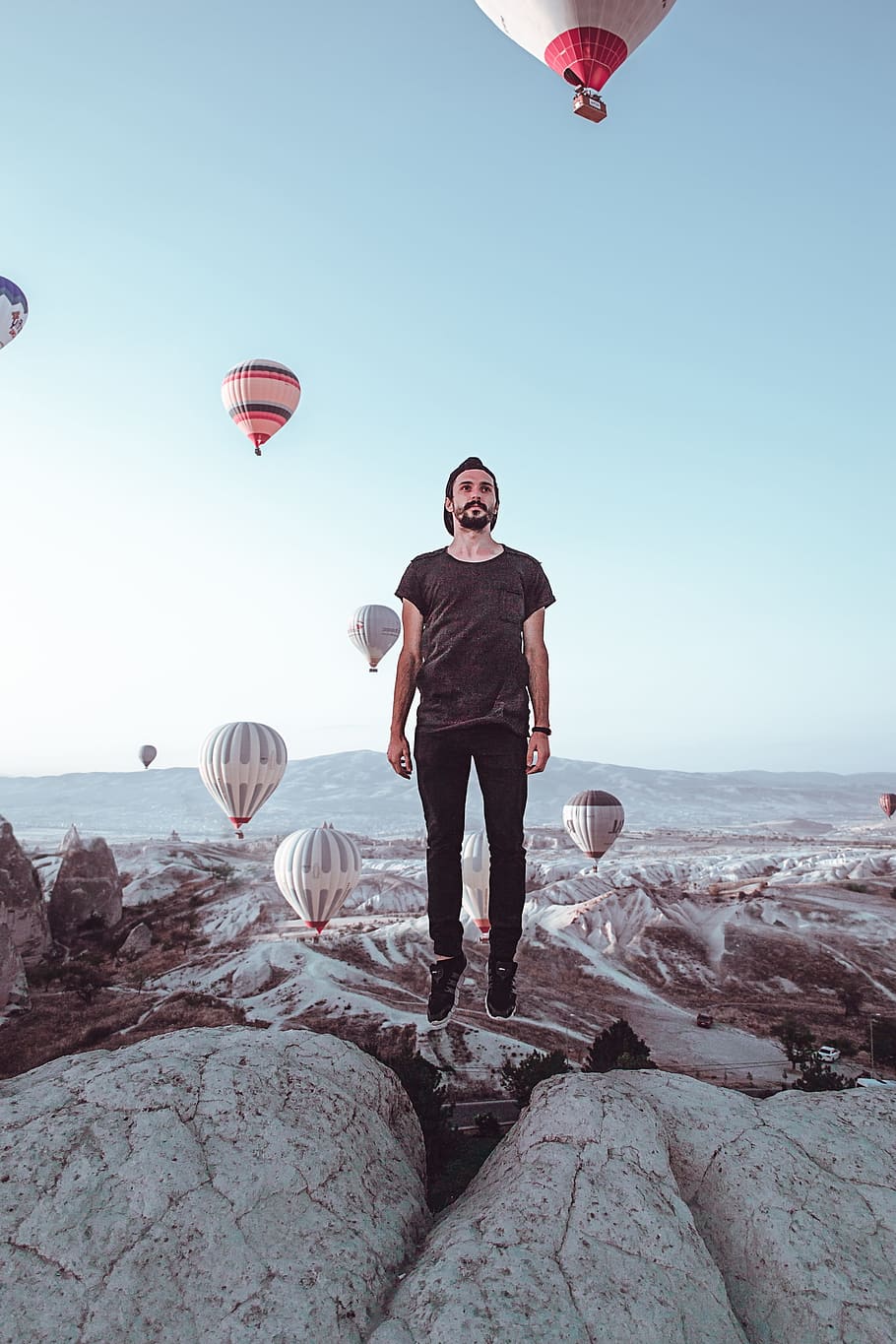 A man standing on top of the ground with balloons in background - Hot air balloons