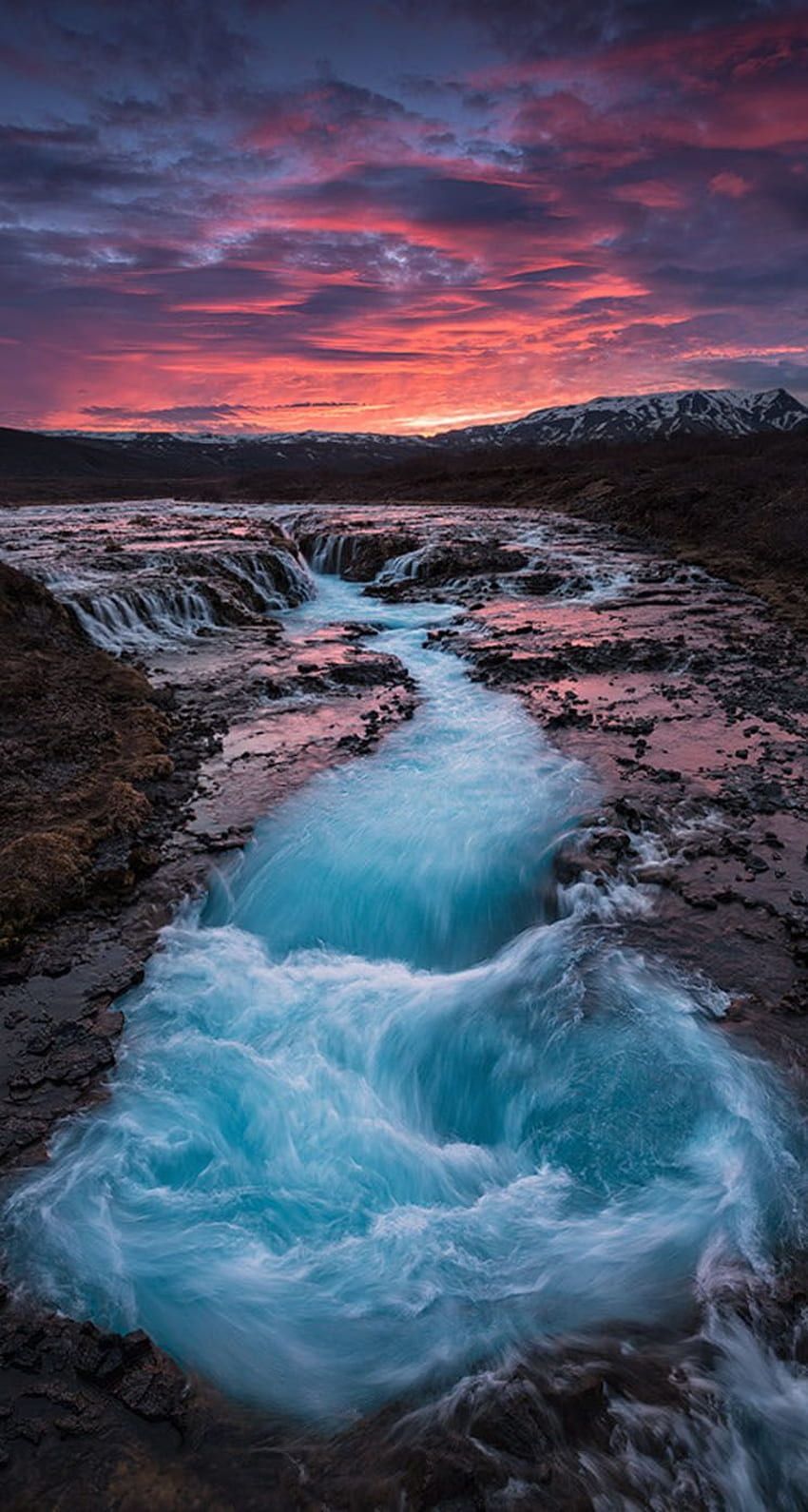 The sky is painted with the colors of the sunset as the river flows through the rocky terrain. - Waterfall