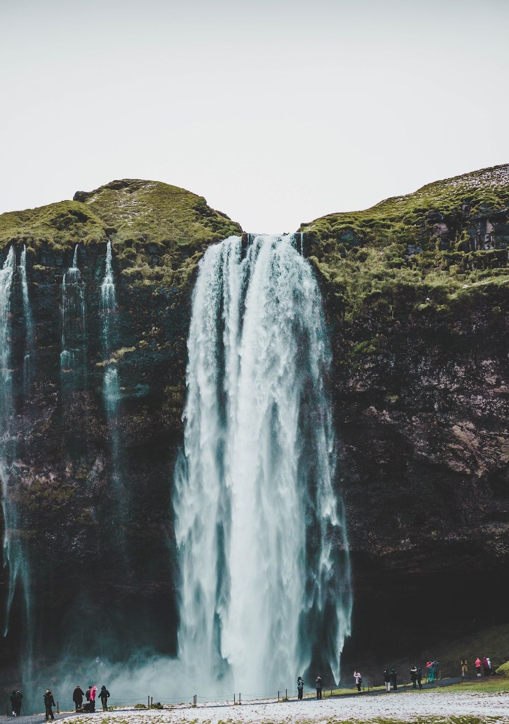 A waterfall with people standing in front of it - Waterfall