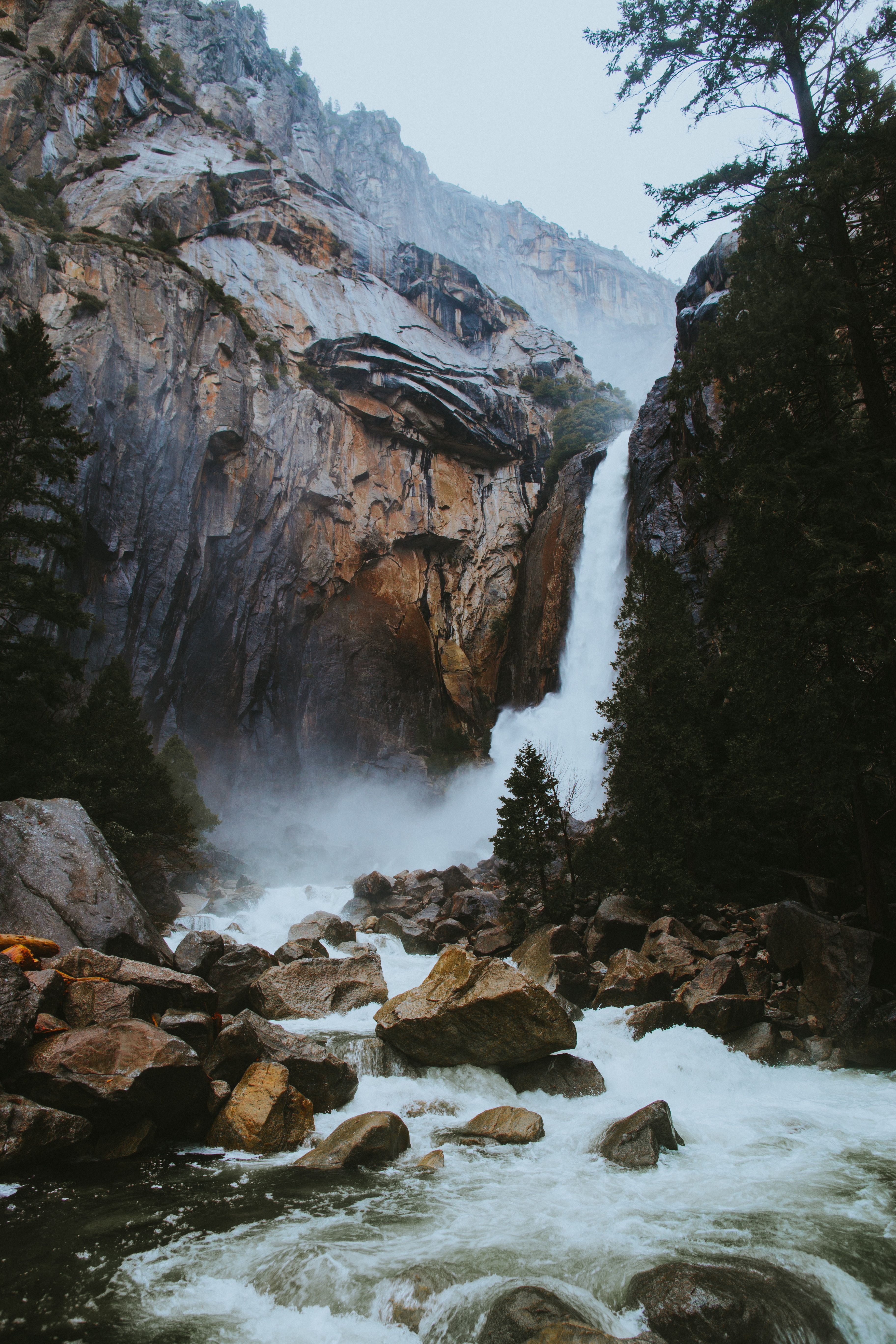 A waterfall cascades down a rocky cliff surrounded by trees. - Waterfall