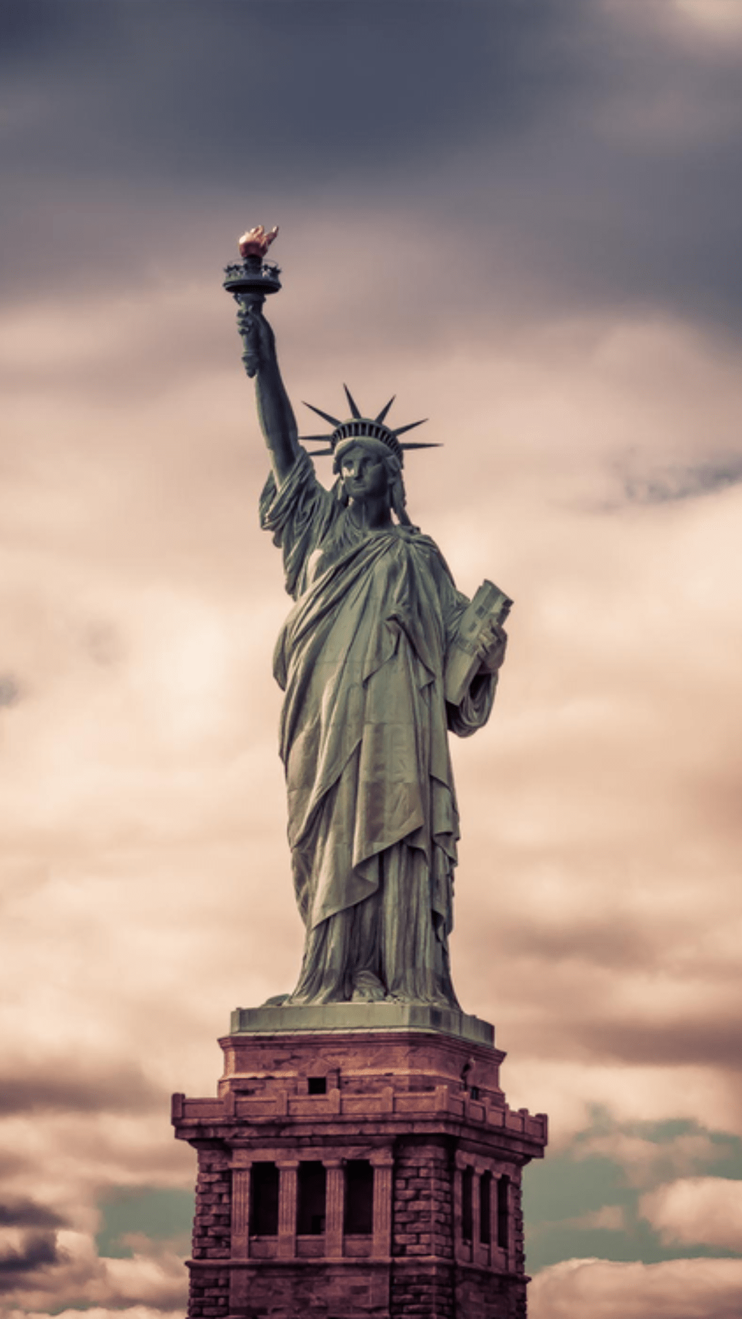 The statue of liberty with a cloudy sky in the background. - Statue