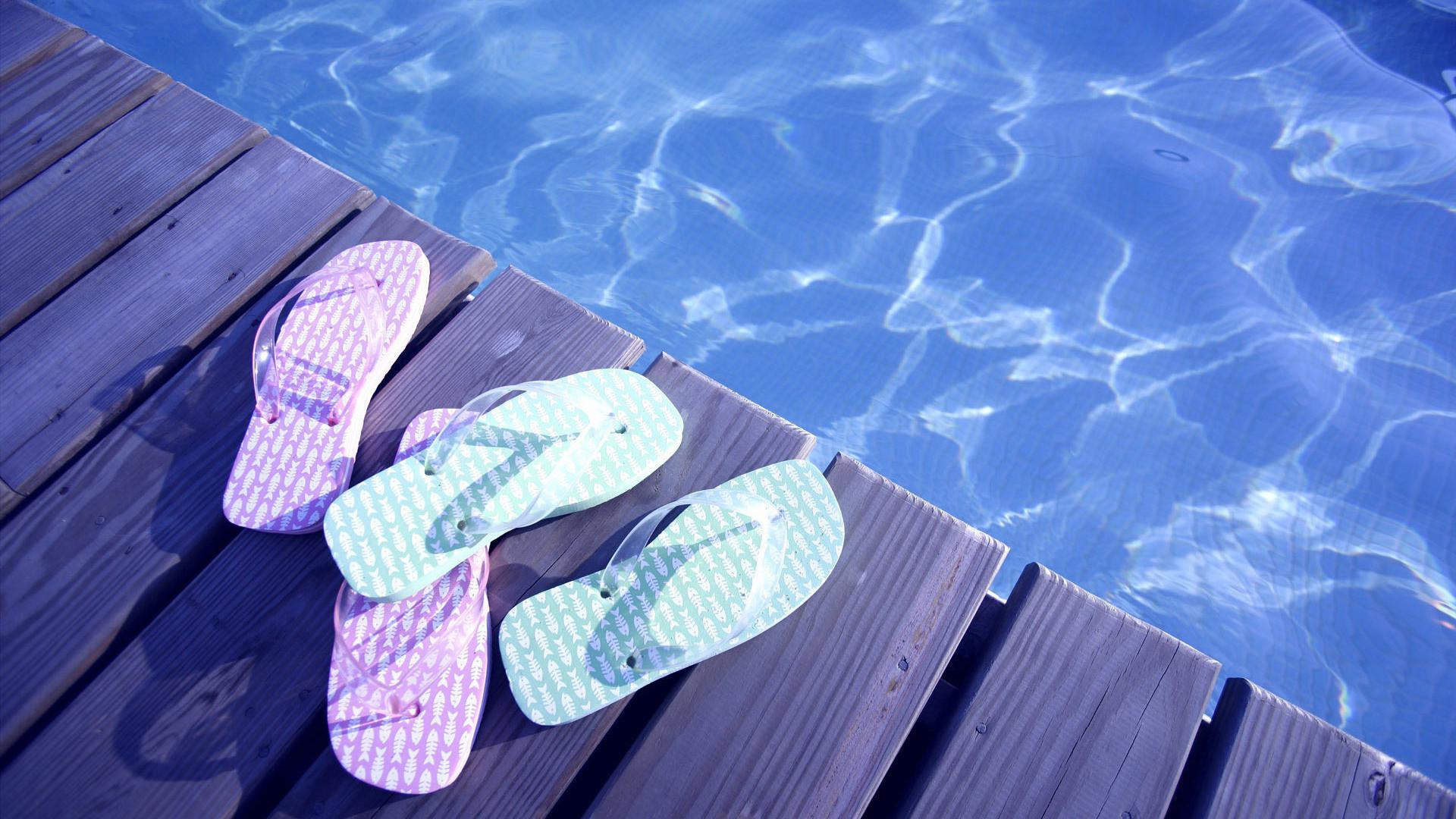 A pair of flip flops sitting on the edge - Swimming pool