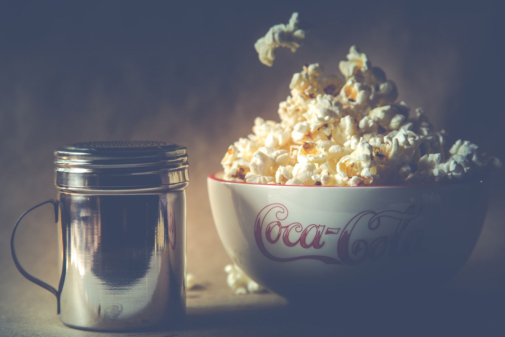 A bowl of popcorn and a bottle of soda on a table. - Popcorn