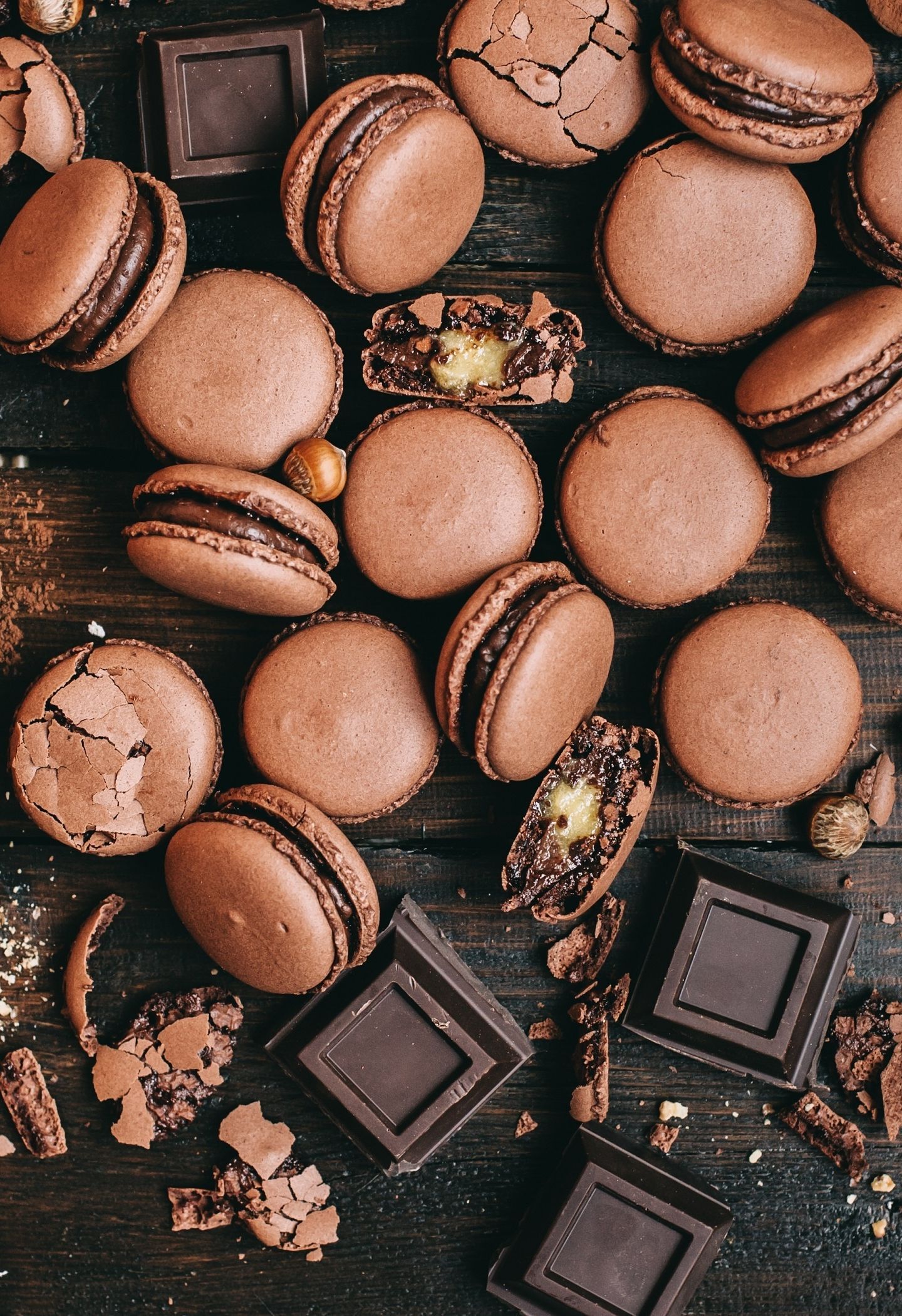 Chocolate macarons with chocolate filling on a wooden table. - Macarons