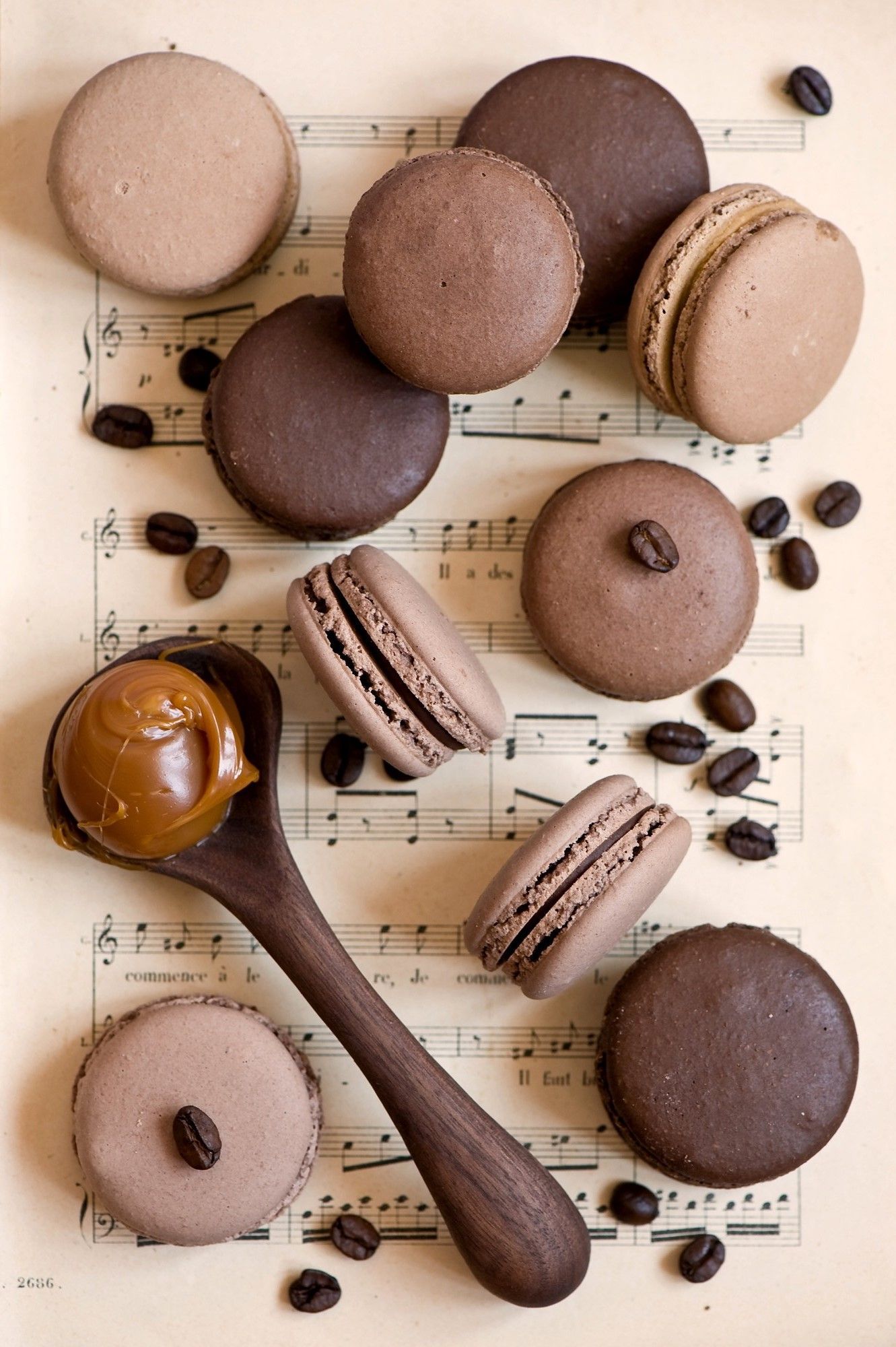 A wooden spoon with chocolate on it next to some cookies - Macarons