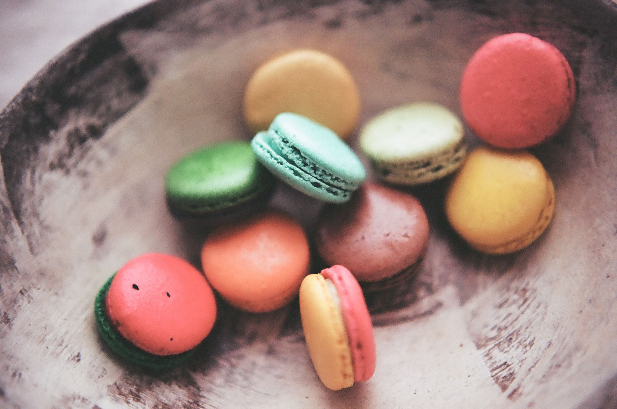 A bowl of colorful macarons on a wooden table. - Macarons