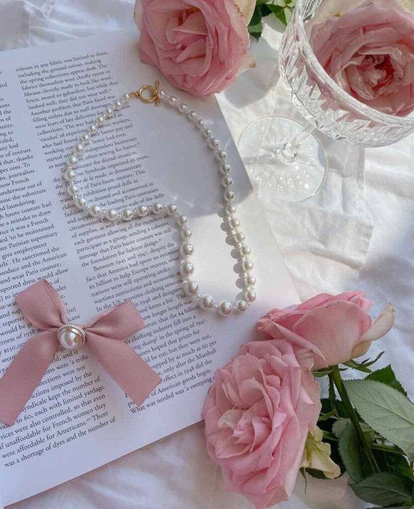 A pearl necklace and roses on top of an open book - Coquette