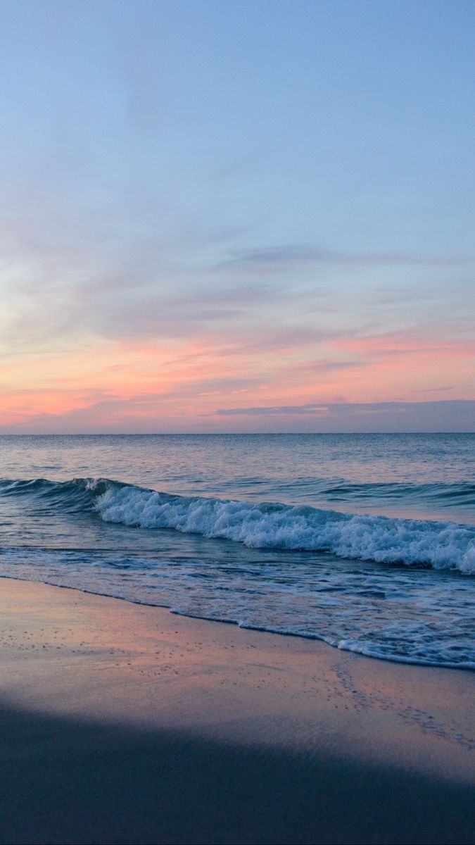 A serene image of a sandy beach and the ocean at sunset. - Coast