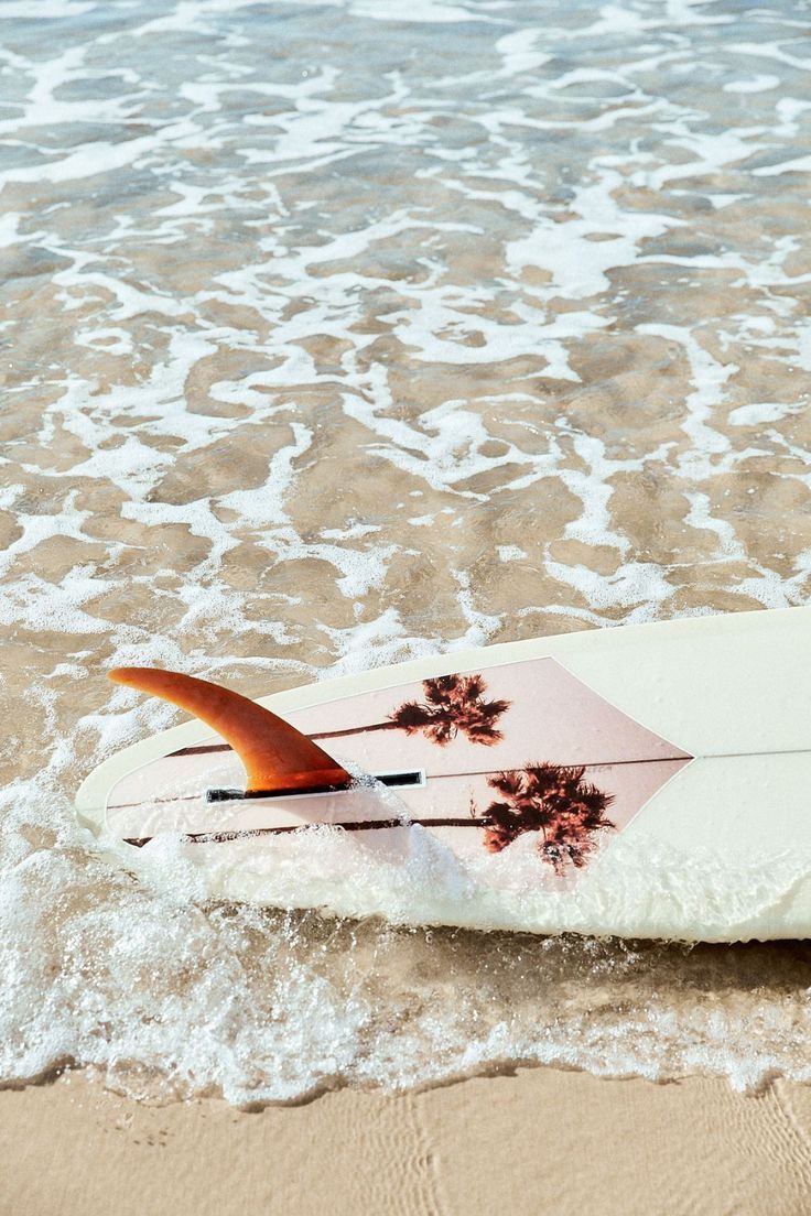 A surfboard on the sand with the ocean in the background - Coast