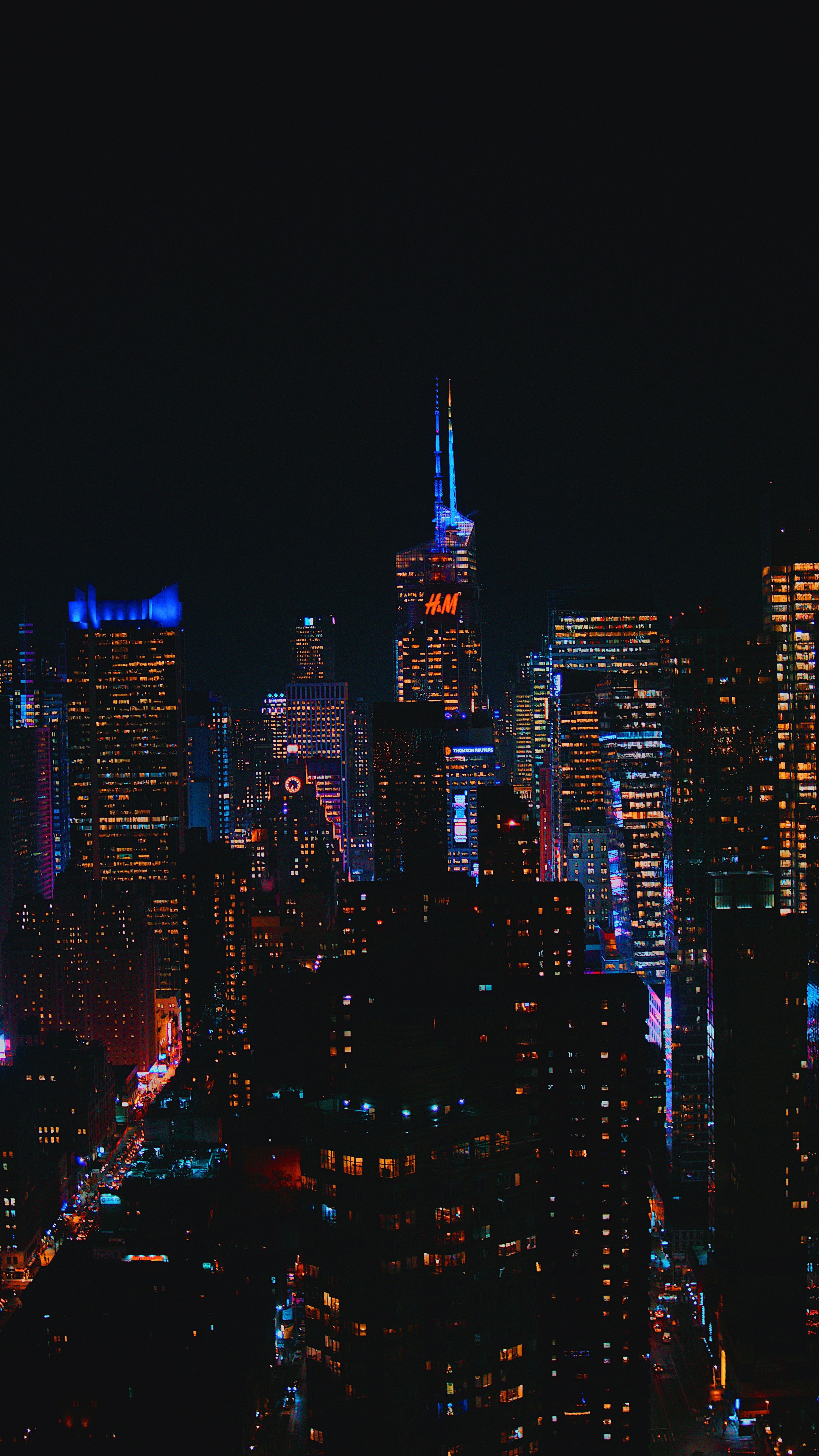 A cityscape at night with skyscrapers lit up in blue, white, and purple. - Skyline, New York