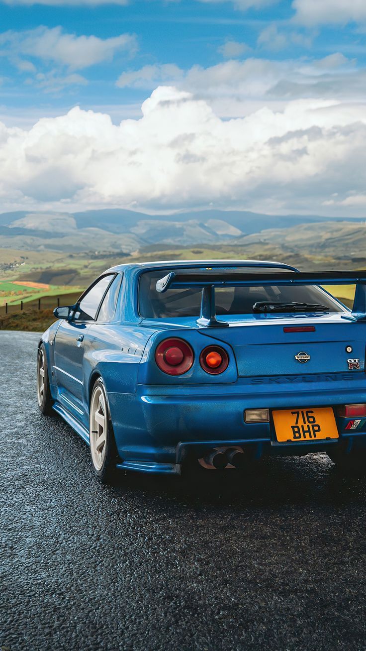 A blue car on the road with mountains in the background - Nissan Skyline