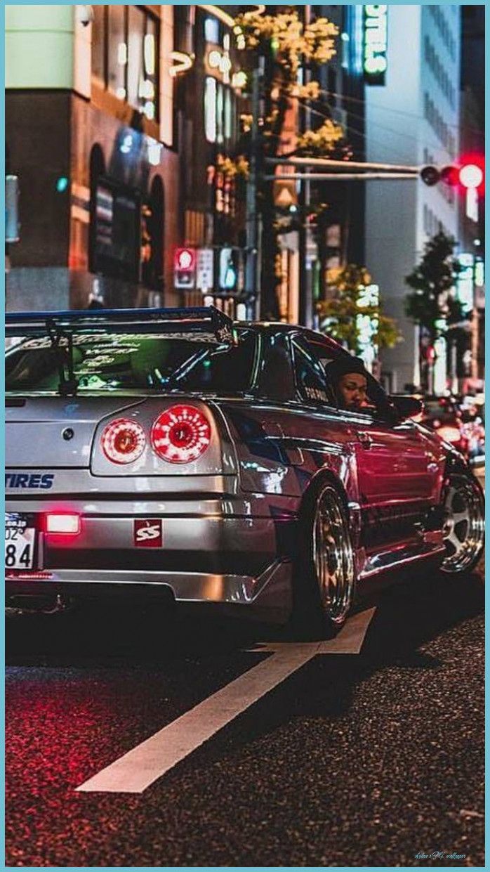 A silver car is parked on the street at night - Nissan Skyline
